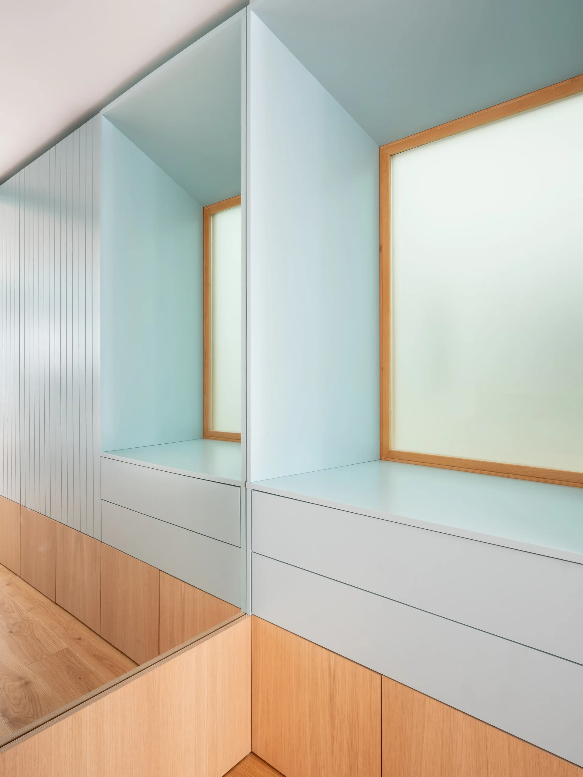 A custom wall unit features matte light blue cabinetry, a built-in niche around a wood-framed window, and warm wood-toned lower cabinets.