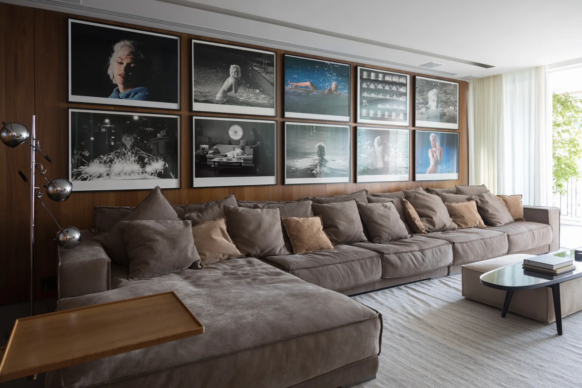 A large brown fabric sectional sofa is positioned in front of a wood-paneled wall featuring a grid of ten framed black and white photographs.
