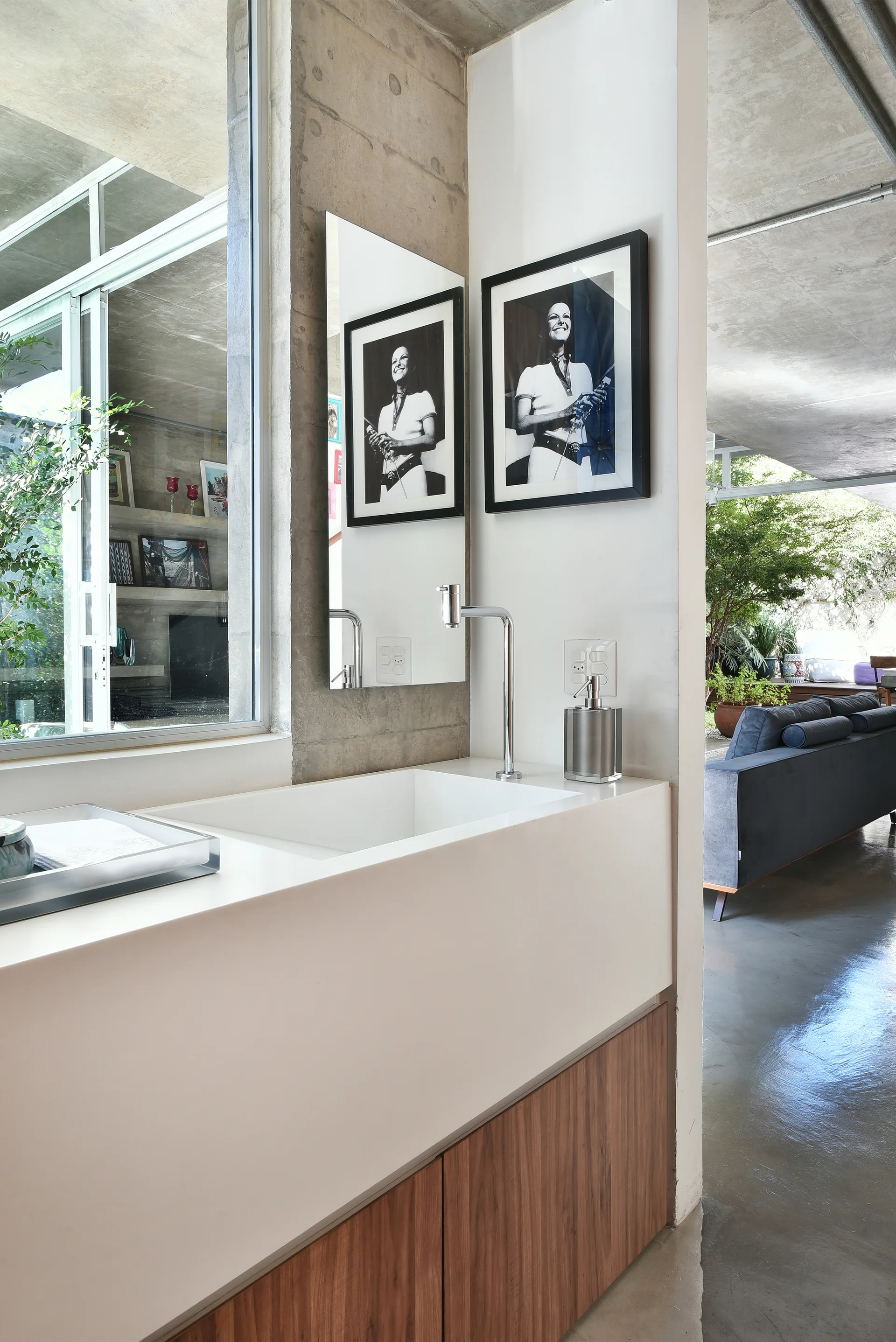 A minimalist bathroom vanity with a white integrated sink, wood-grain cabinets, and a tall mirror set against a raw concrete wall.