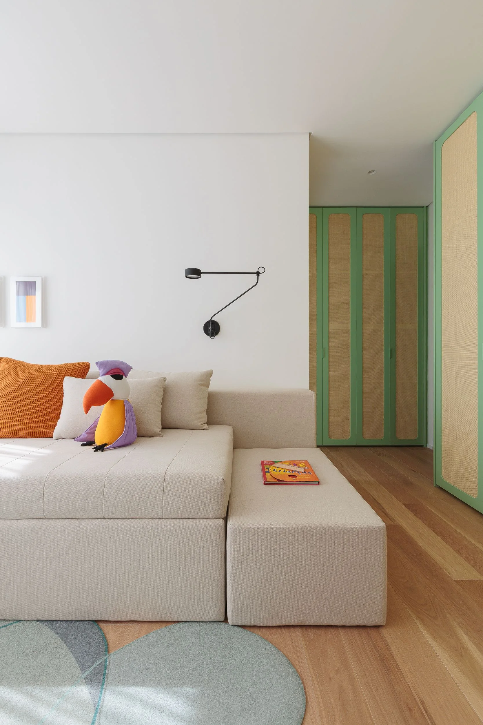 A minimalist beige modular sofa is accented with colorful pillows next to built-in green wardrobe doors with natural cane panels.