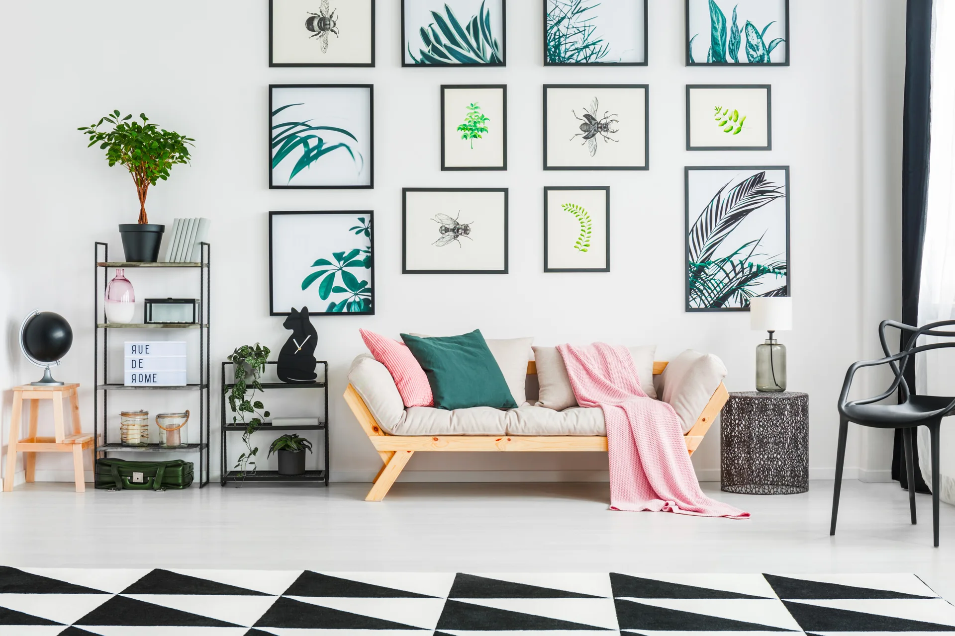 A light wood sofa sits on a geometric rug beneath a large gallery wall of black-framed botanical art prints.