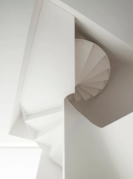 A low-angle view of a sculptural white spiral staircase with sharp geometric edges and a smooth matte finish.