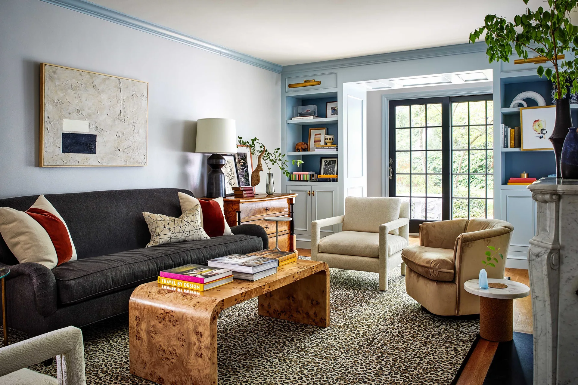 A living room features a charcoal sofa, a burl wood waterfall coffee table, and blue painted built-in shelving next to a black French door.