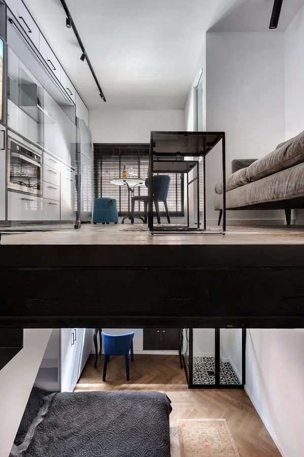 A modern split-level apartment view showing an upper kitchen and living area above a lower bedroom space with wood herringbone flooring.