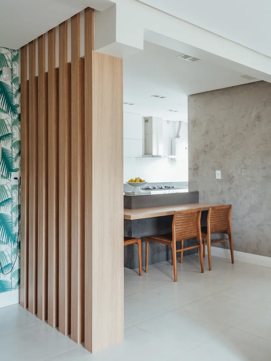 A modern kitchen featuring a wooden slat room divider, a textured grey accent wall, and a kitchen island with two wooden chairs.