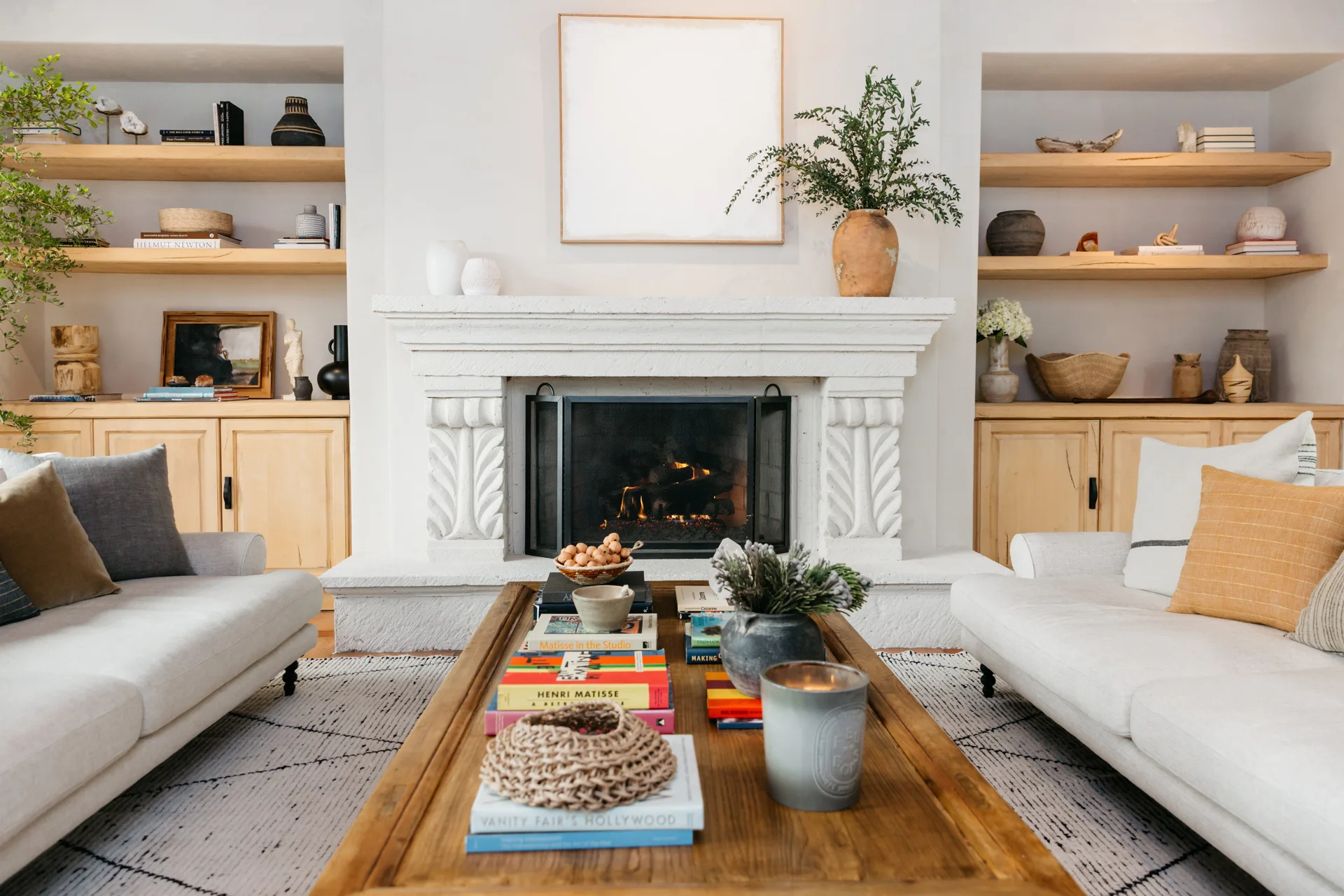 A light living room featuring a central white stone fireplace, flanked by recessed wood shelving and two cream sofas facing each other.