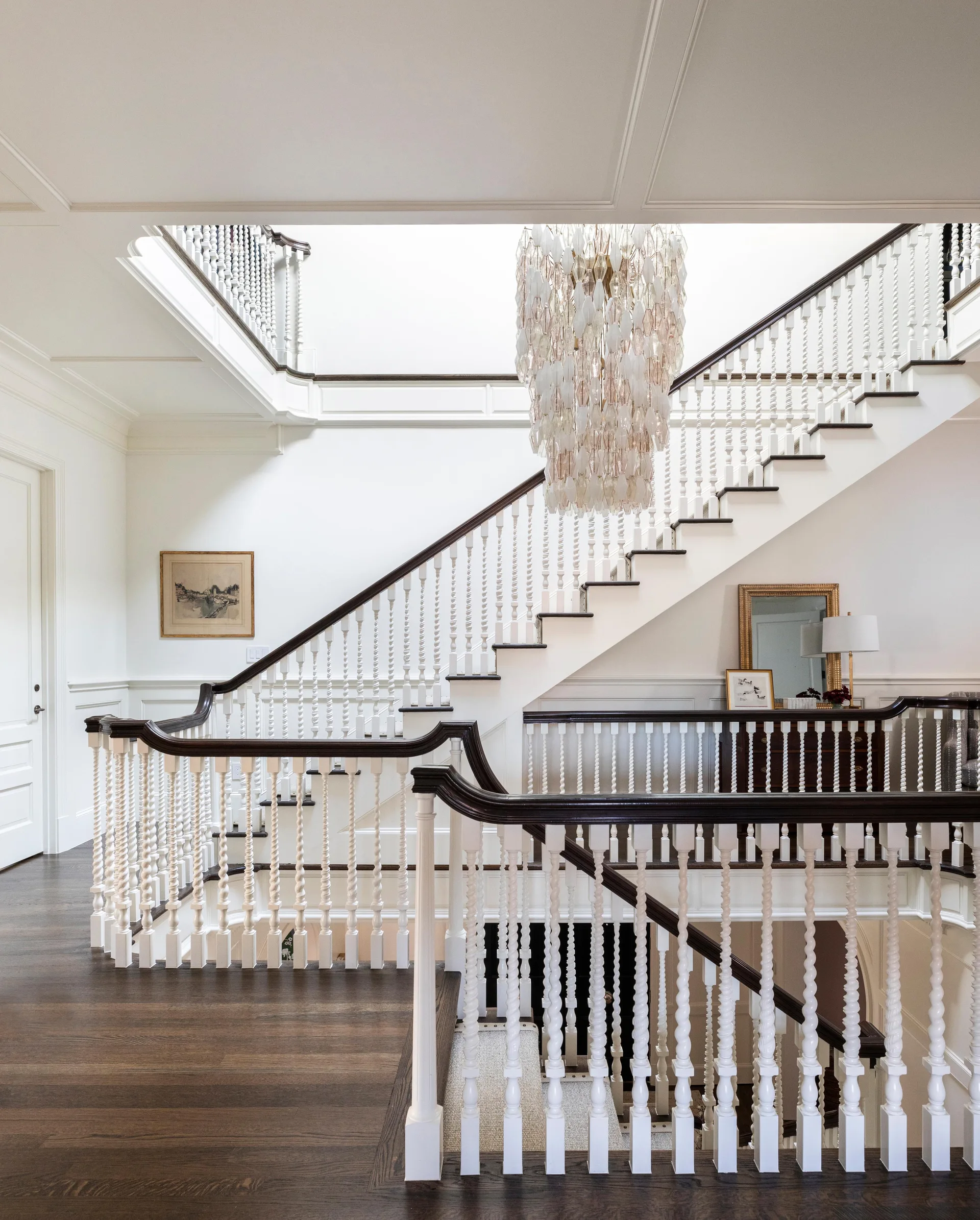 A multi-level traditional staircase features white barley twist balusters, dark wood handrails, and a hanging cascading capiz shell chandelier.