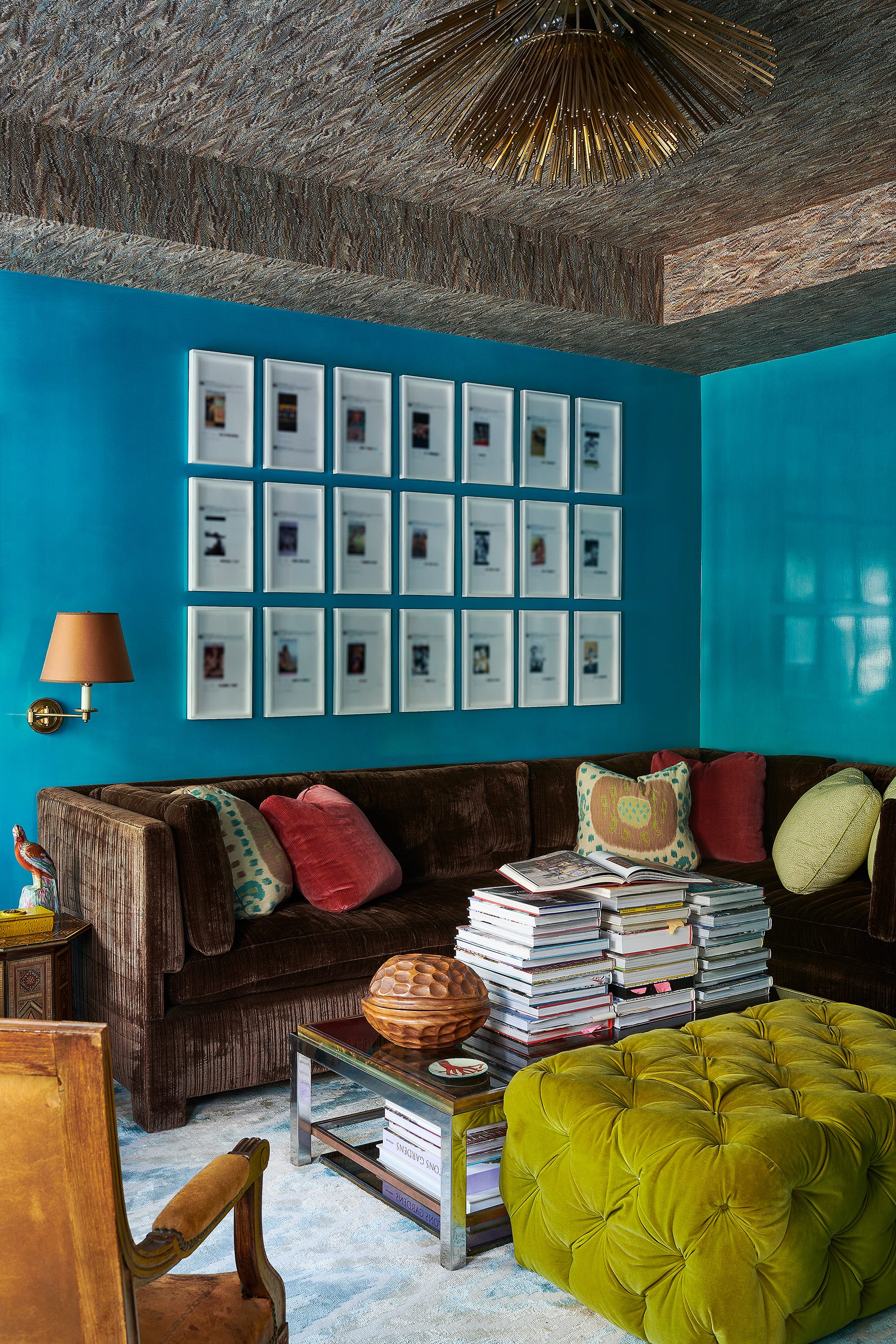 A living room features a dark brown velvet sofa, bright blue walls with a grid gallery wall, and a tufted green velvet ottoman.