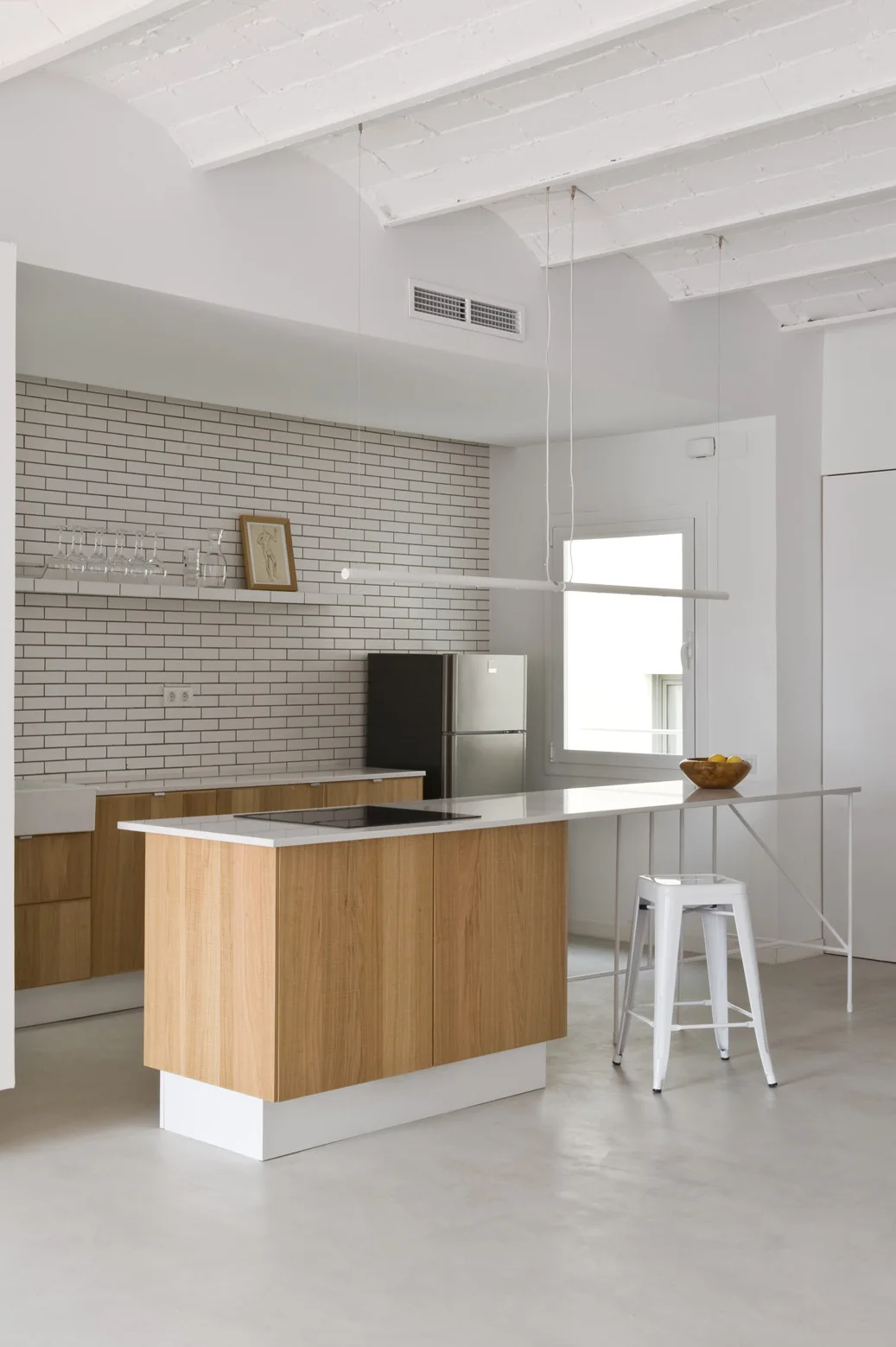 A minimalist kitchen features a light wood island with a white countertop extending into a bar, backed by a full subway tile wall.