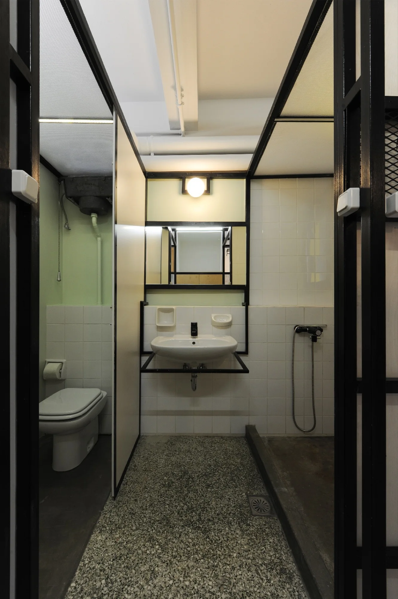 Industrial bathroom with a white sink and toilet partitioned by black metal framing on a speckled terrazzo floor.