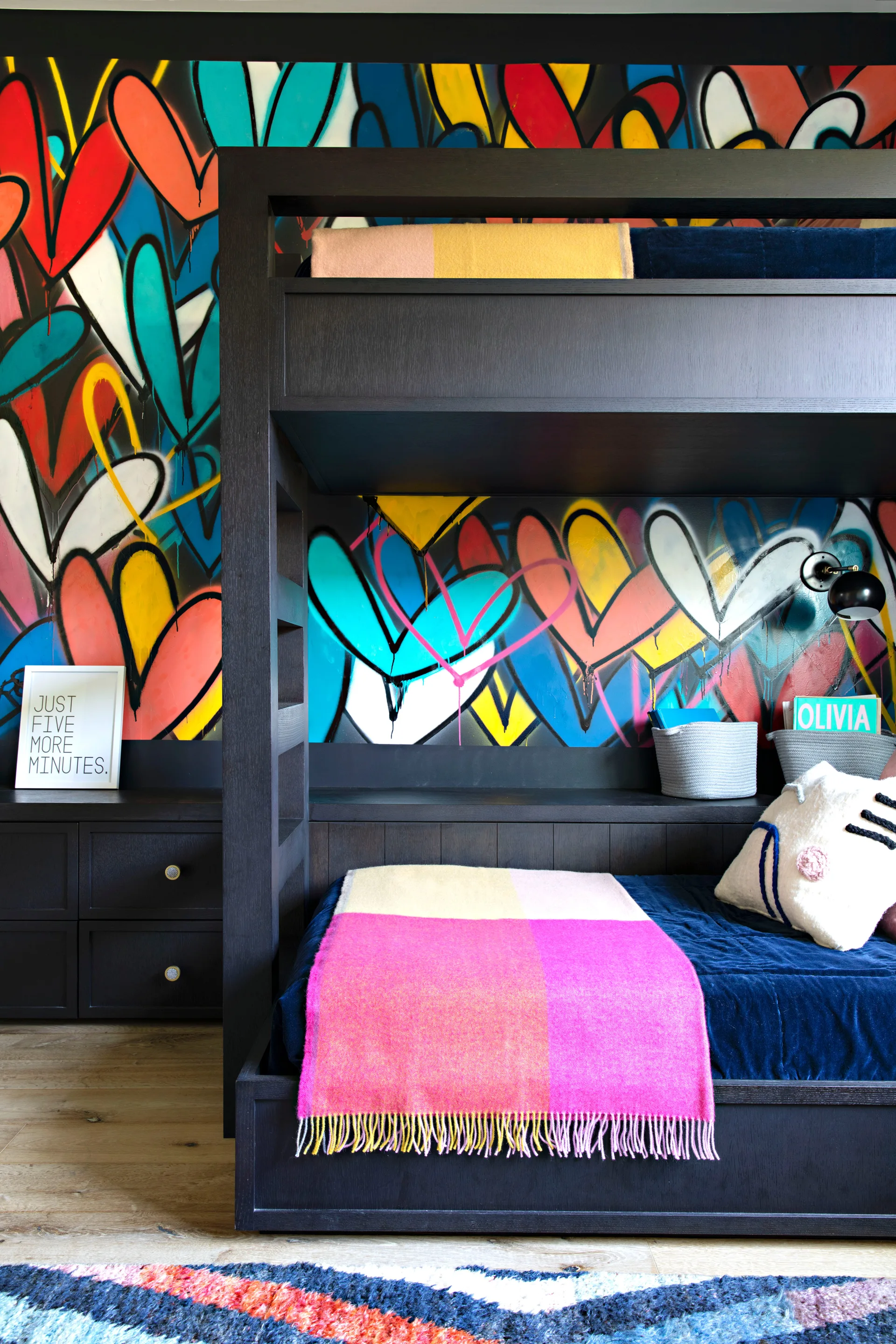 A dark wood bunk bed stands against a colorful graffiti wall covered in painted hearts next to built-in storage drawers in a child's bedroom.