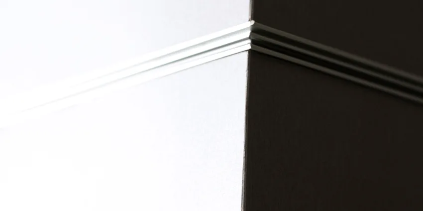 A close-up view of a sharp corner joint between a white matte panel and a dark brown panel separated by a thin silver metal trim piece.