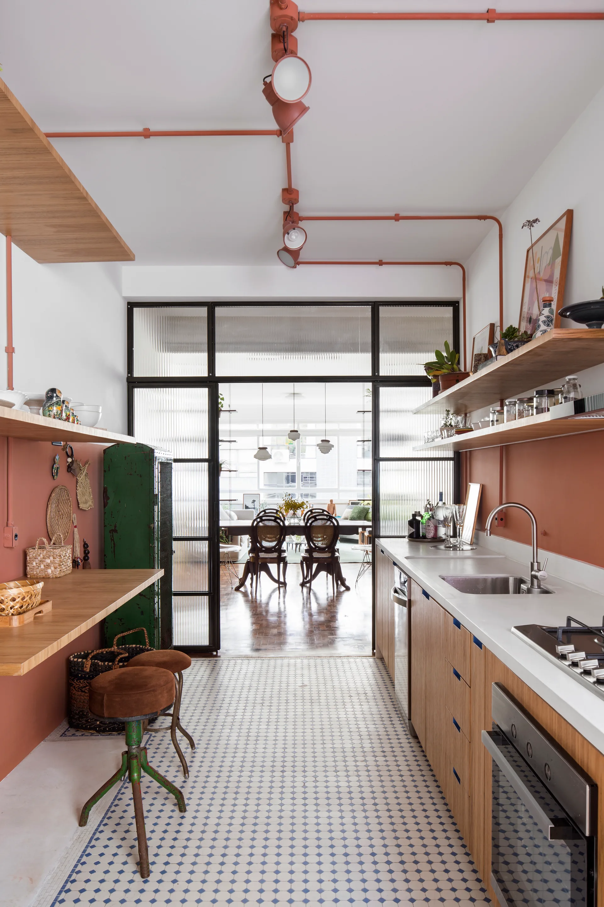 A narrow galley kitchen with coral walls, wood-toned cabinets, and geometric tile floors leading to a reeded glass divider.