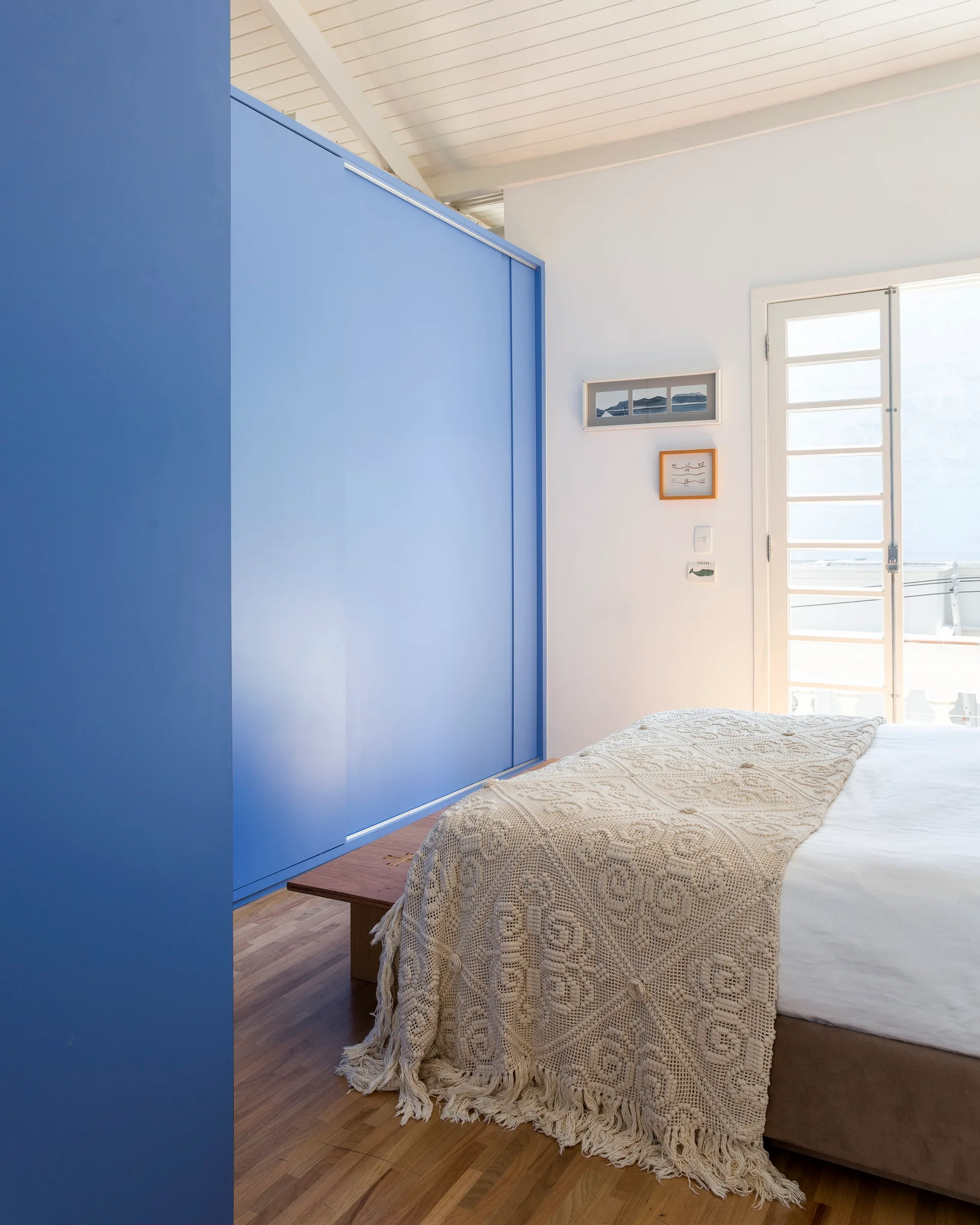 A bedroom features a large blue sliding door wardrobe, a bed with a textured crochet throw, and a white glass-paneled door leading outside.