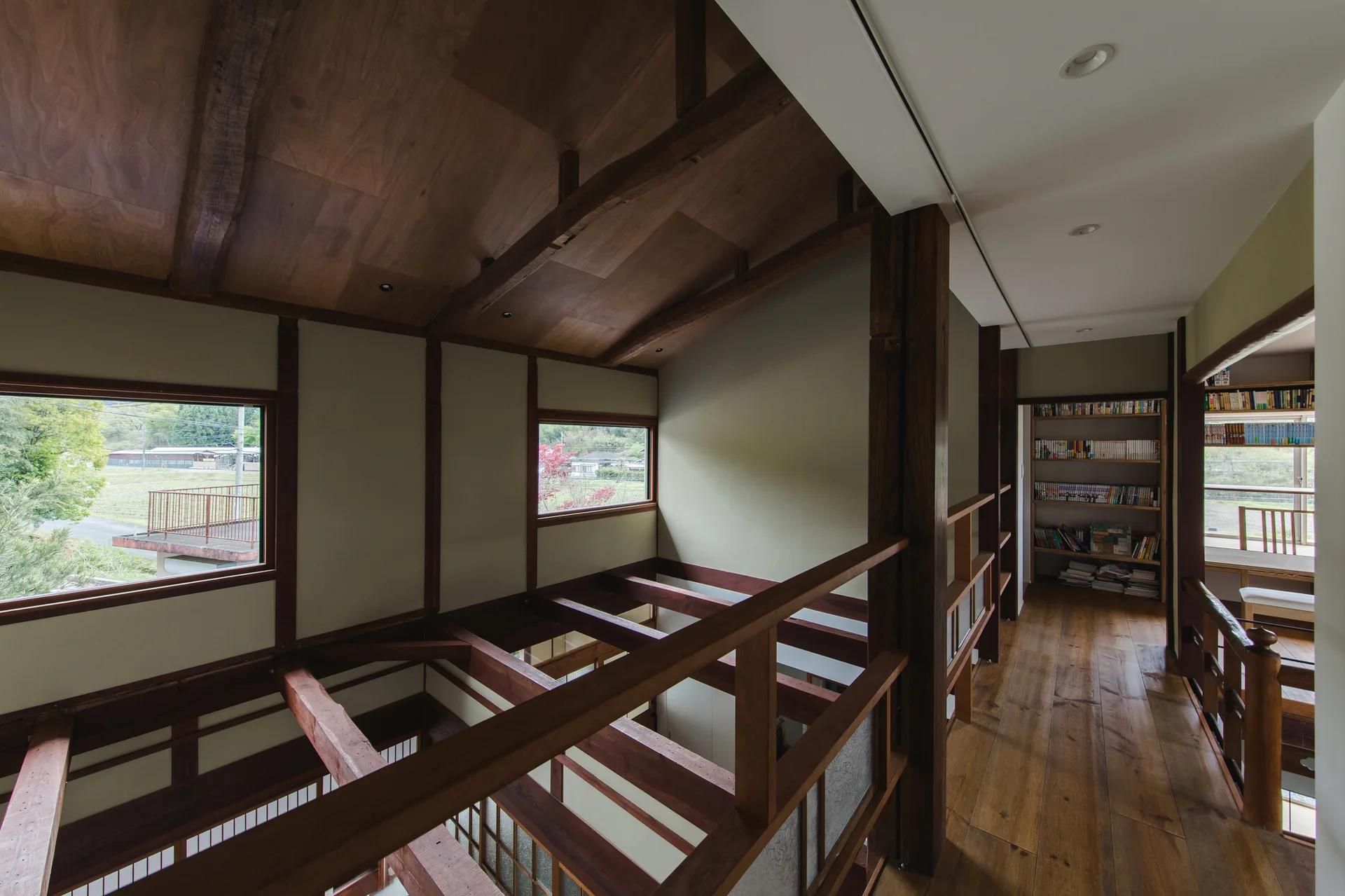 A modern Japanese landing with exposed timber beams, vaulted wood ceiling, wood plank floors, and a built-in bookshelf.