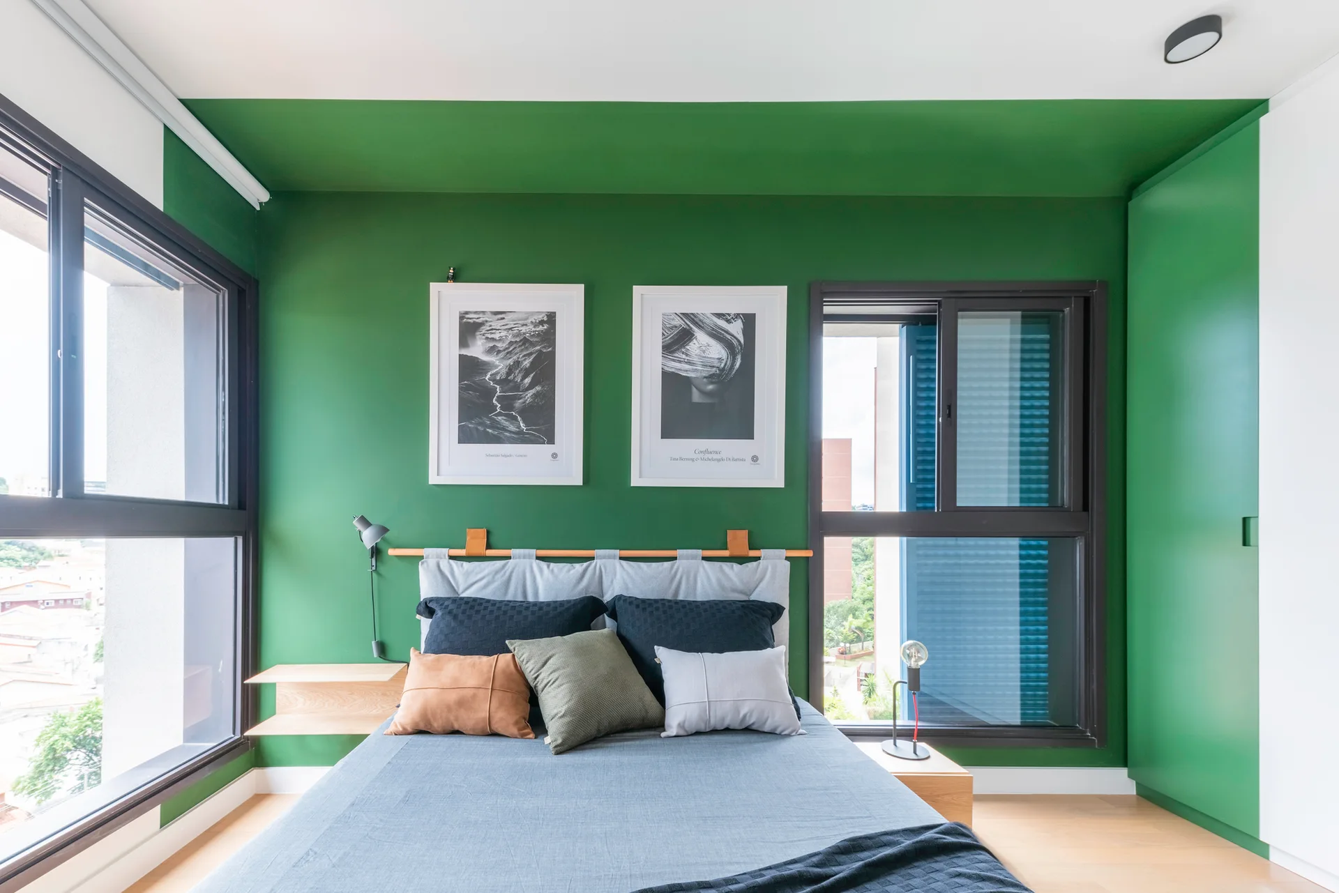A modern bedroom with a bold green painted wall and ceiling, a grey upholstered bed with decorative pillows, and floating wooden nightstands.