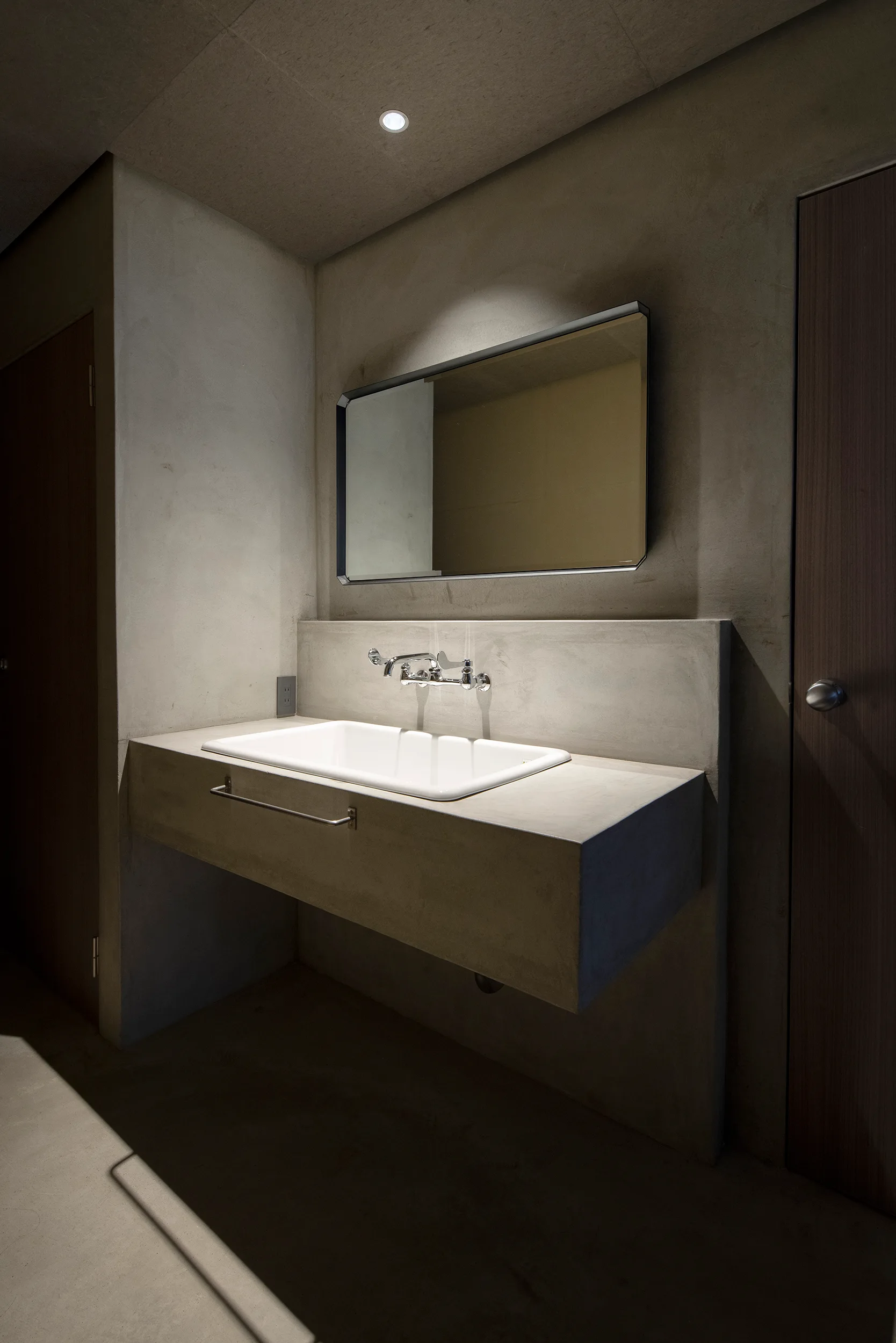 A minimalist bathroom featuring a grey concrete floating vanity with a white ceramic sink, a wall-mounted chrome faucet, and a rectangular mirror.