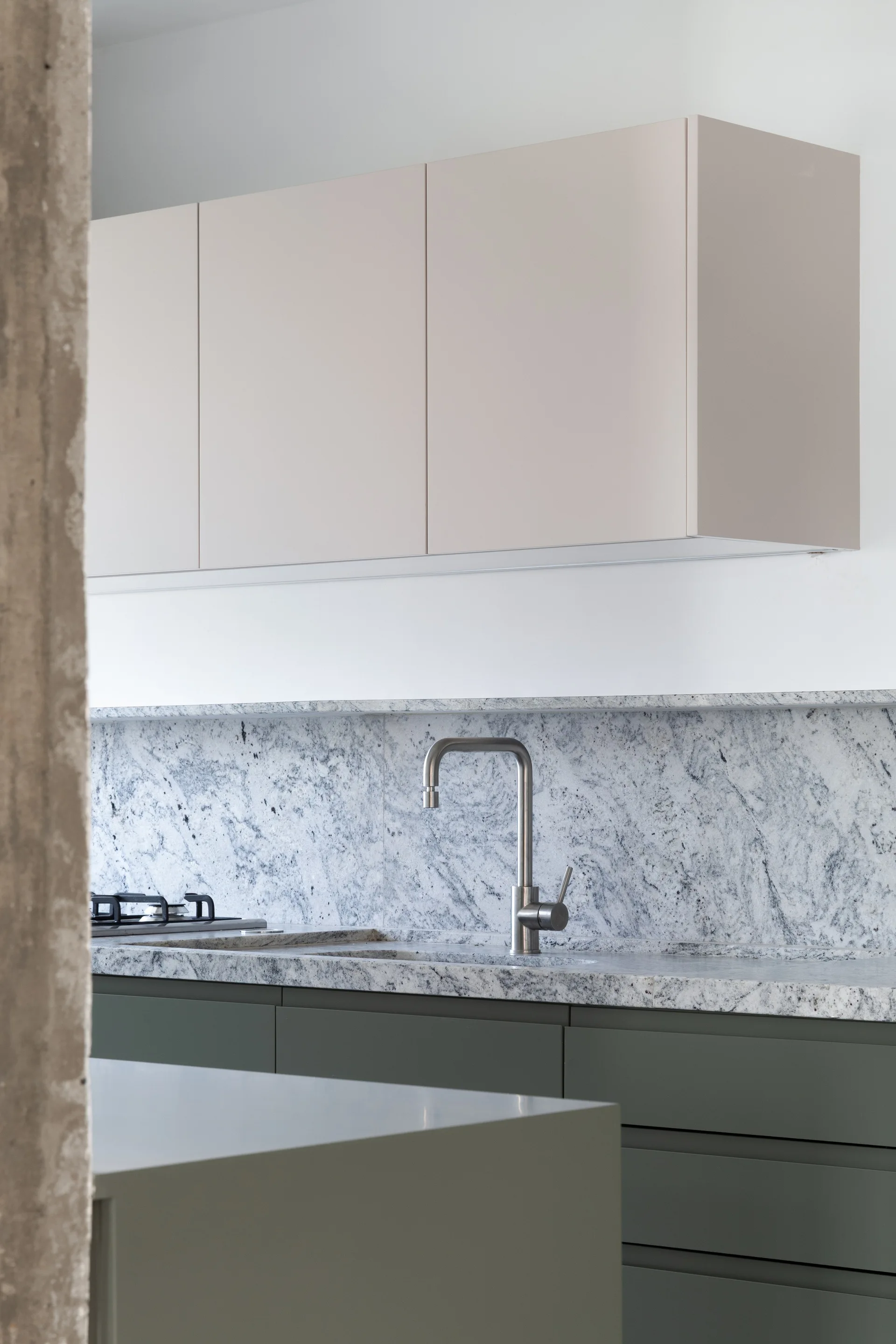 A modern kitchen features sage green lower cabinets, light beige upper cabinets, a veined stone backsplash, and a brushed metal faucet.