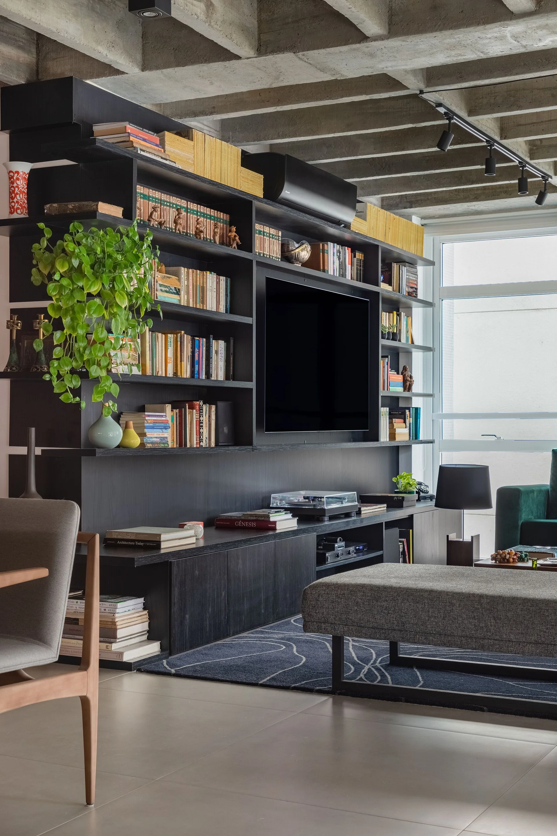A contemporary living room featuring a large black built-in shelving unit filled with books beneath an exposed concrete waffle ceiling.