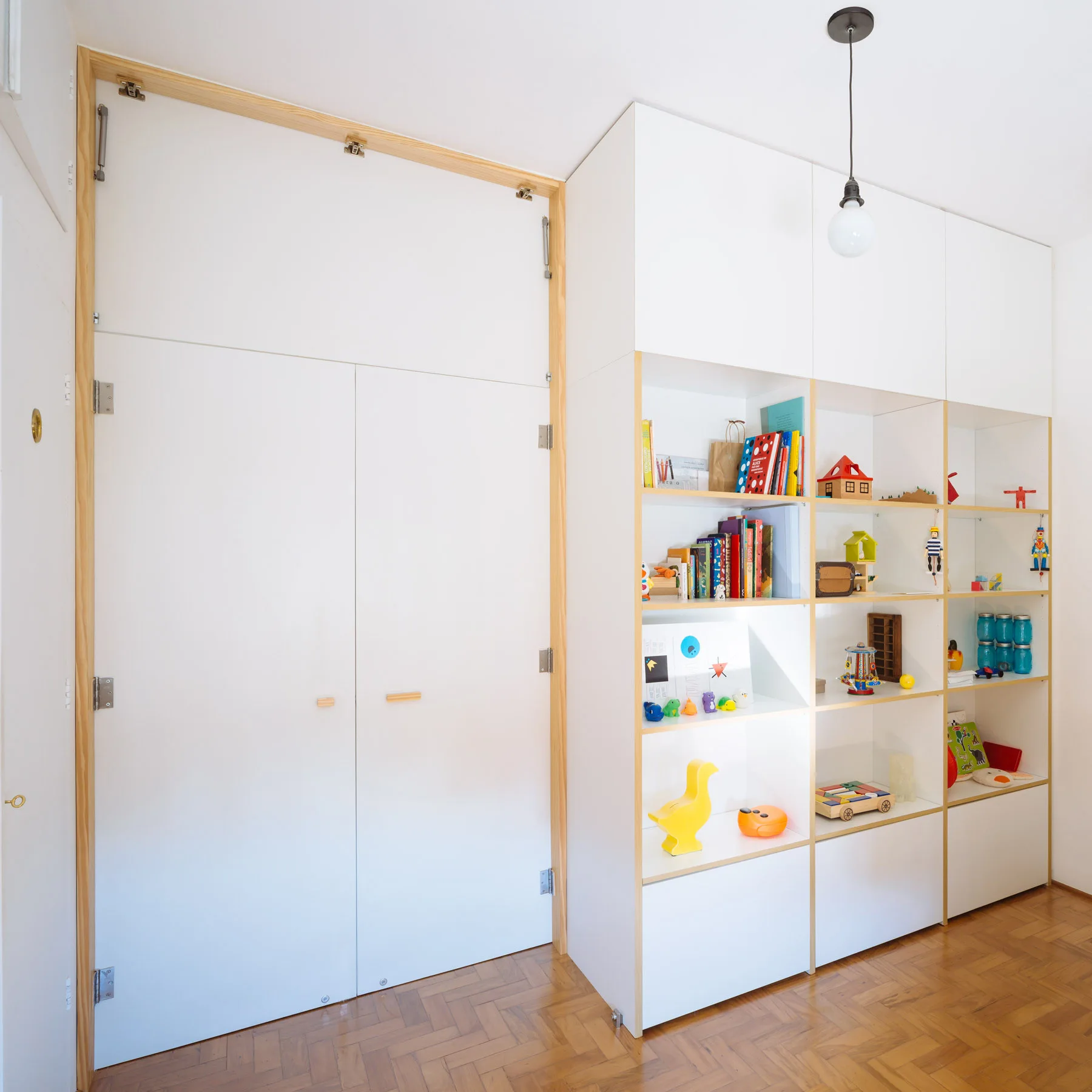 A white built-in storage unit featuring a closet and open shelving with wood trim sits on a herringbone floor.