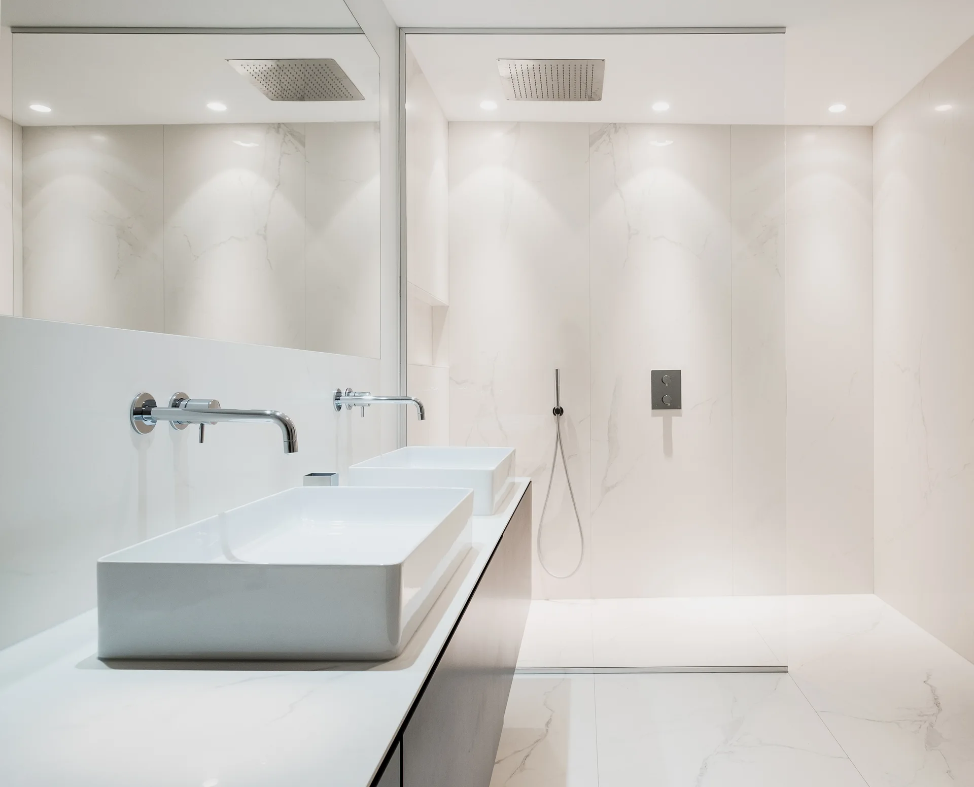 A modern white bathroom features a floating double vanity with two rectangular vessel sinks and a glass-enclosed walk-in shower.