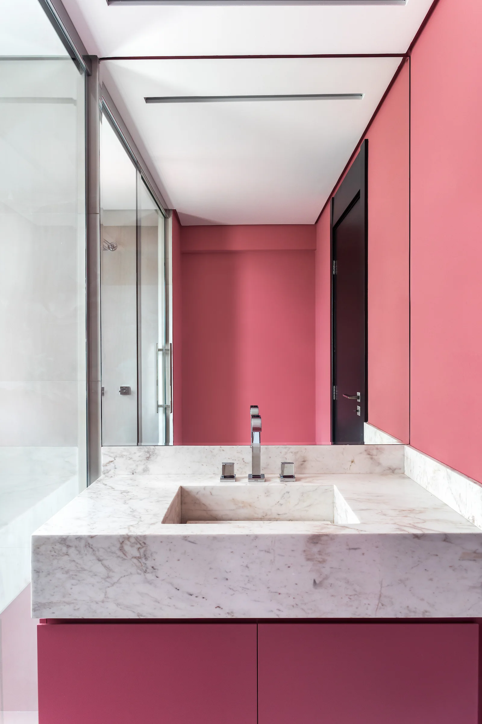 A modern pink bathroom features an integrated marble sink on a pink vanity with a large mirror reflecting a glass shower enclosure.