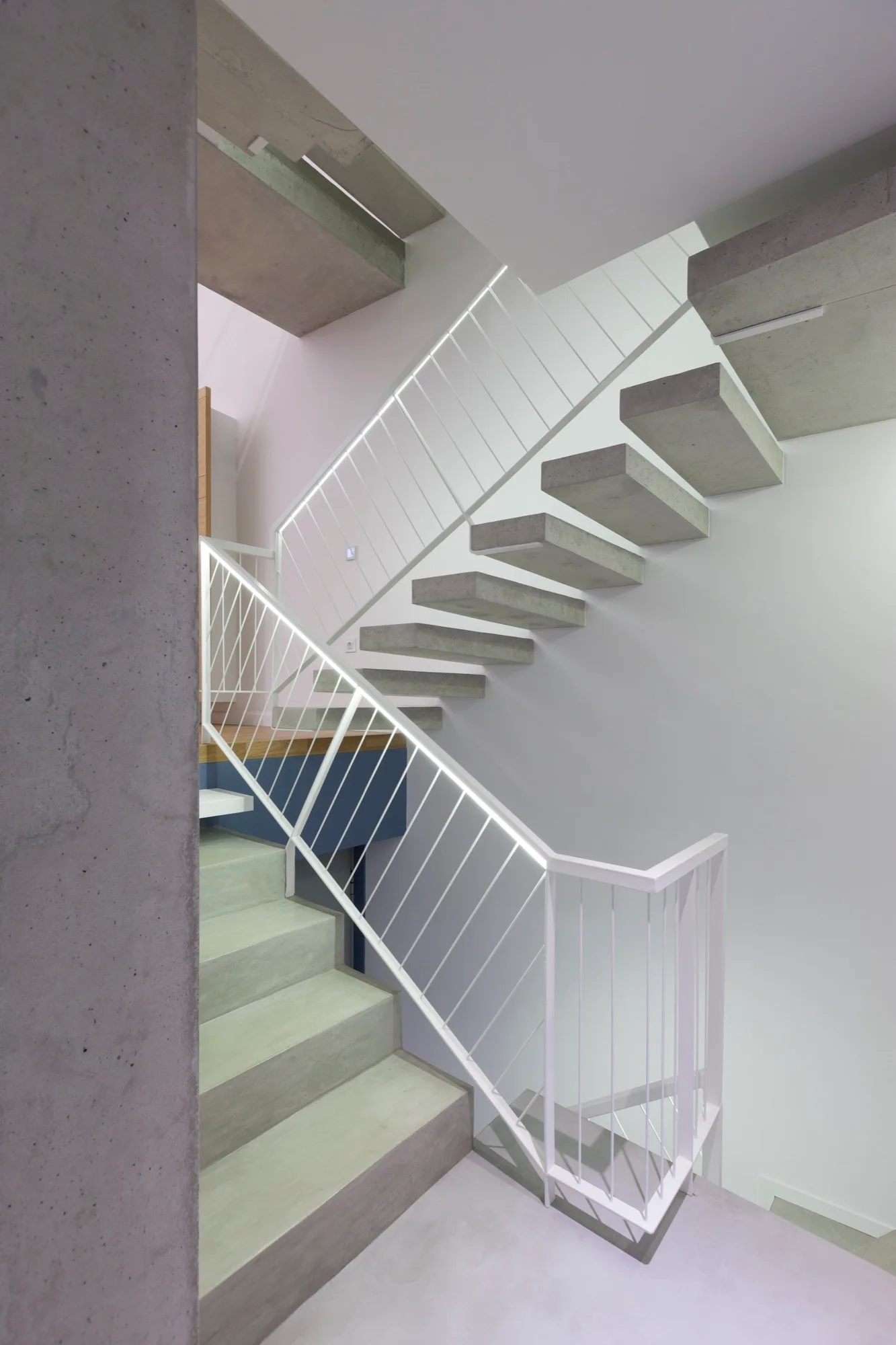 A modern floating staircase features raw concrete steps and a minimalist white metal railing against bright white walls.