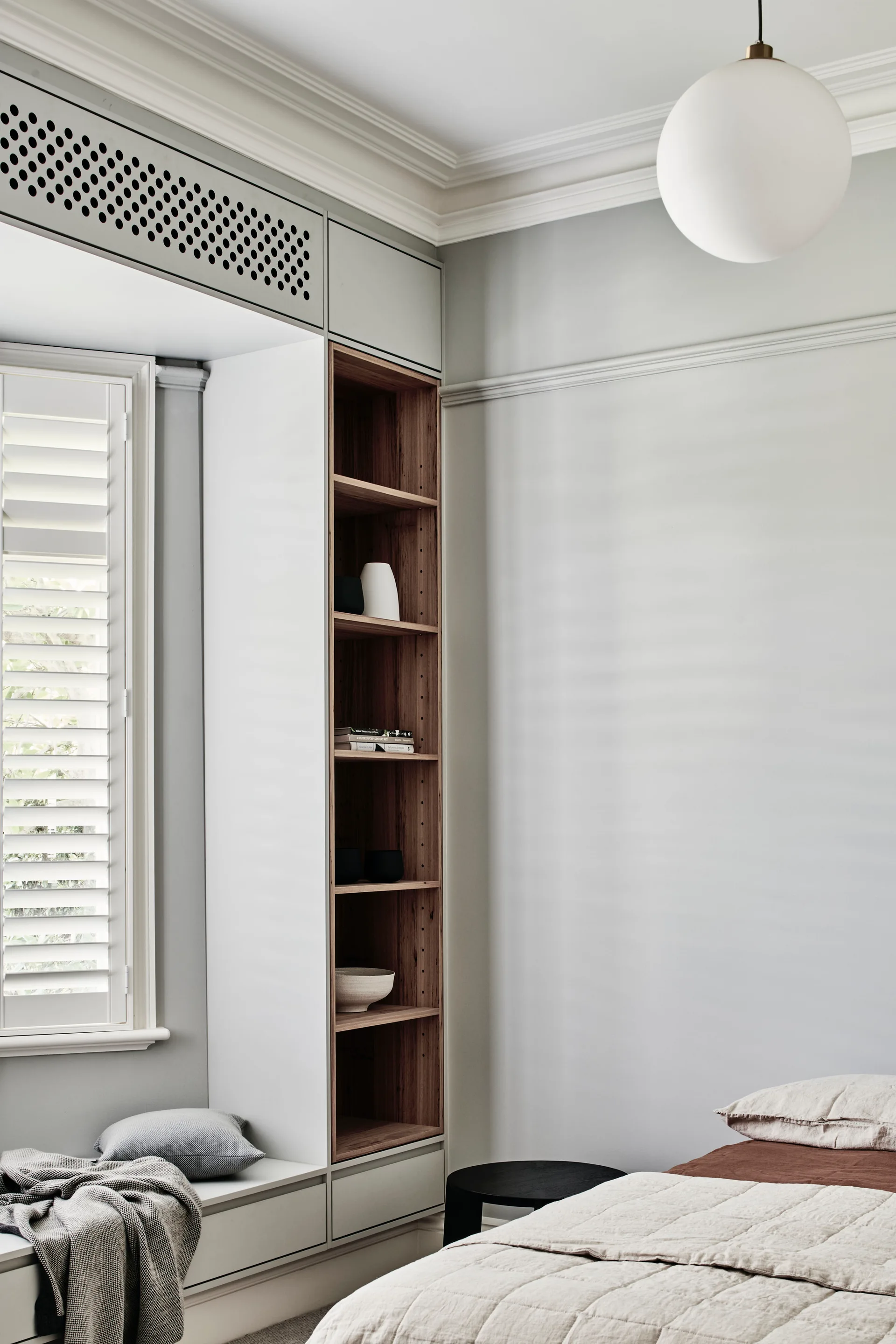 A bedroom corner featuring light grey built-in cabinetry with an integrated window seat, open wood shelving, and a white globe pendant light.