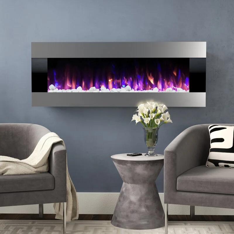 A wall-mounted electric fireplace with purple flames is flanked by two gray armchairs and an hourglass side table holding white flowers.