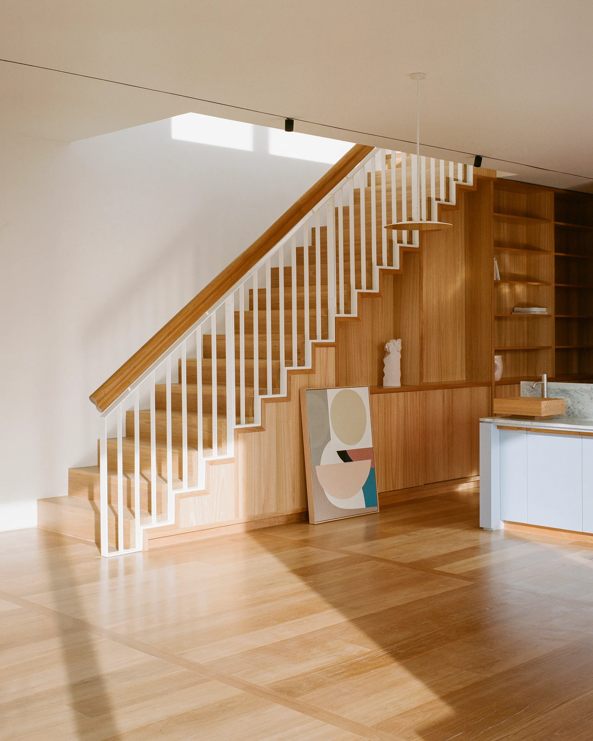 A minimalist wooden staircase with white railings features integrated oak under-stair storage cabinets on parquet floors.