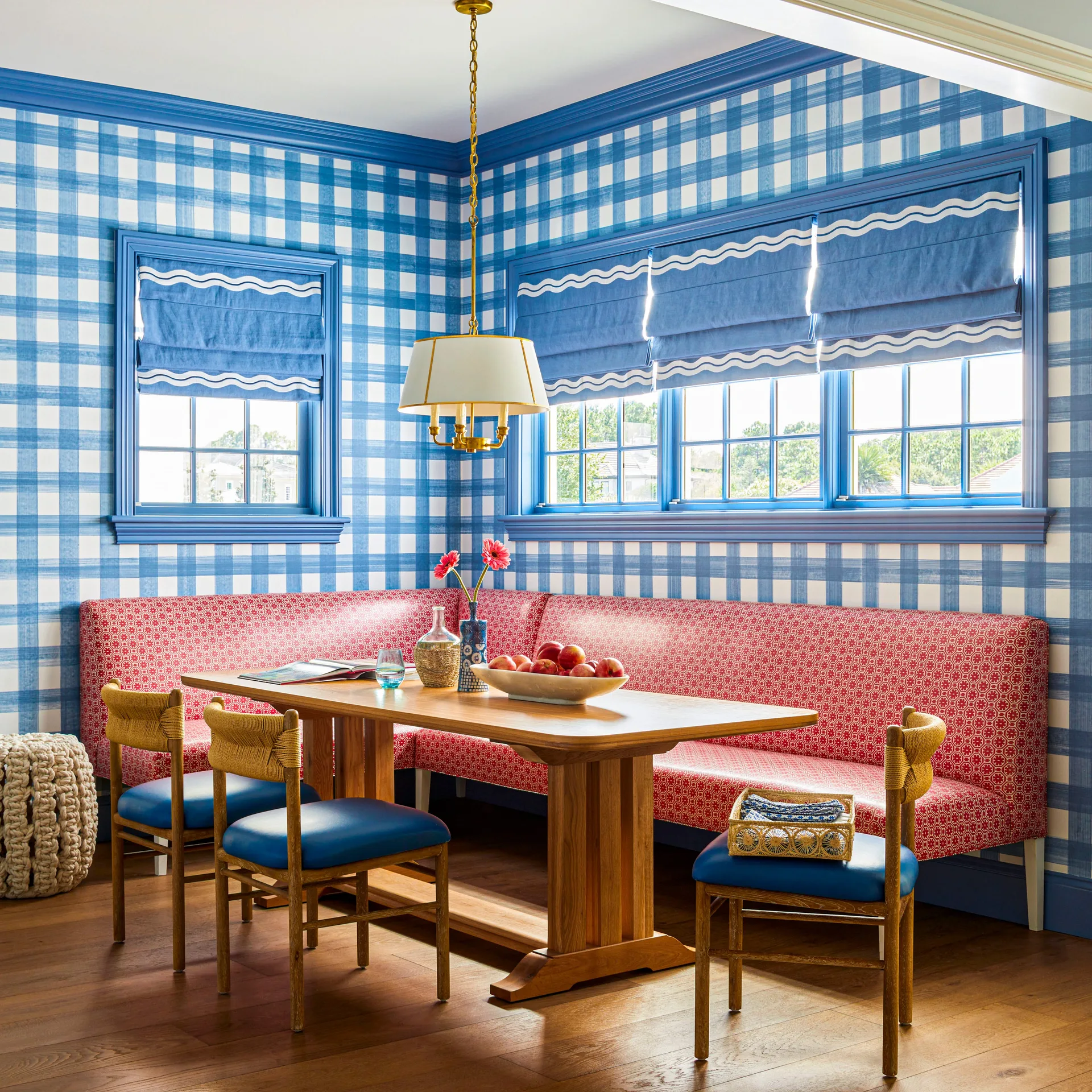 A corner dining nook features a red patterned banquette under windows with blue trim, set against blue and white checkered wallpaper.