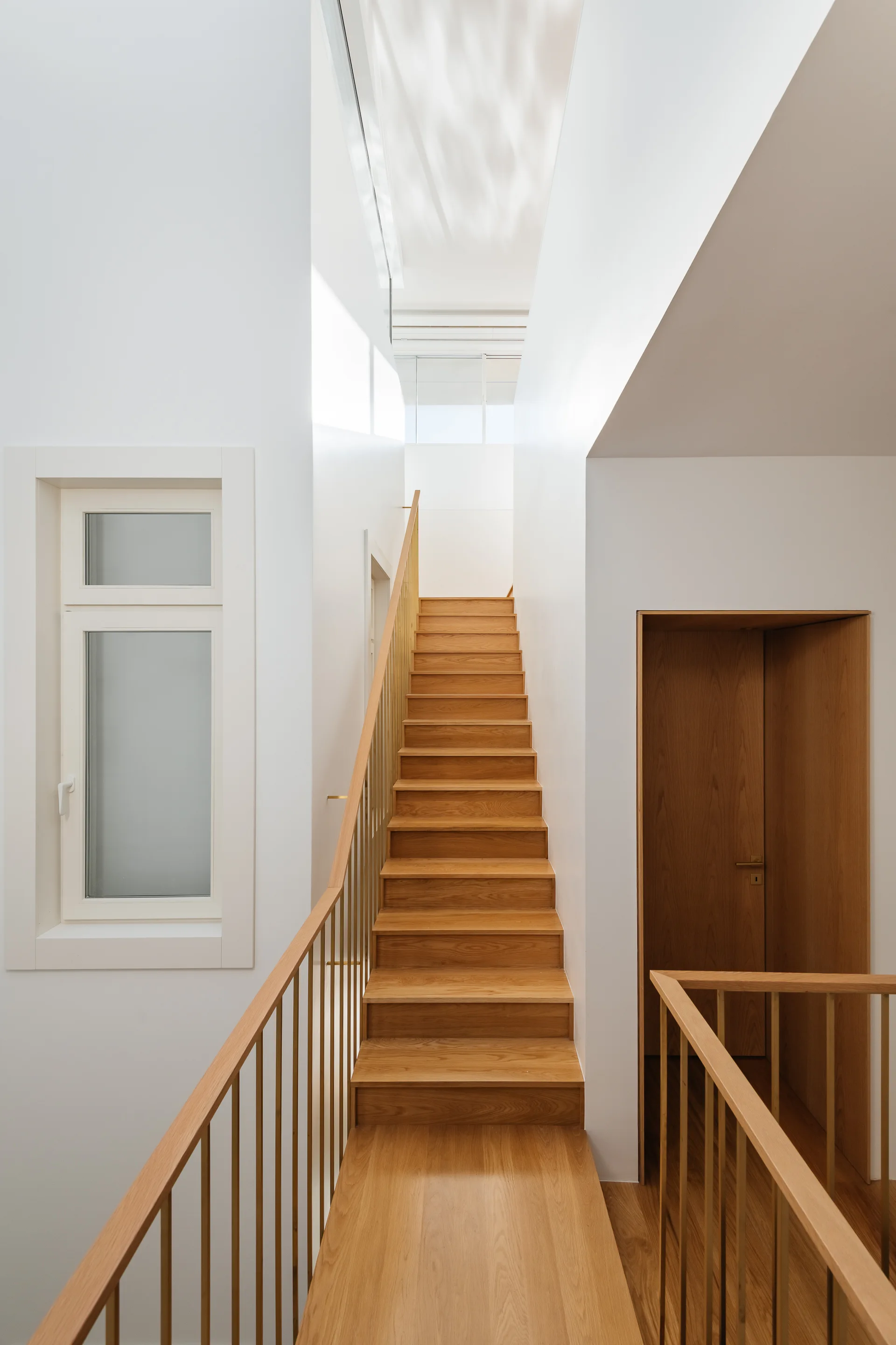 A minimalist modern staircase featuring light wood treads, a thin metal railing, and smooth white walls.