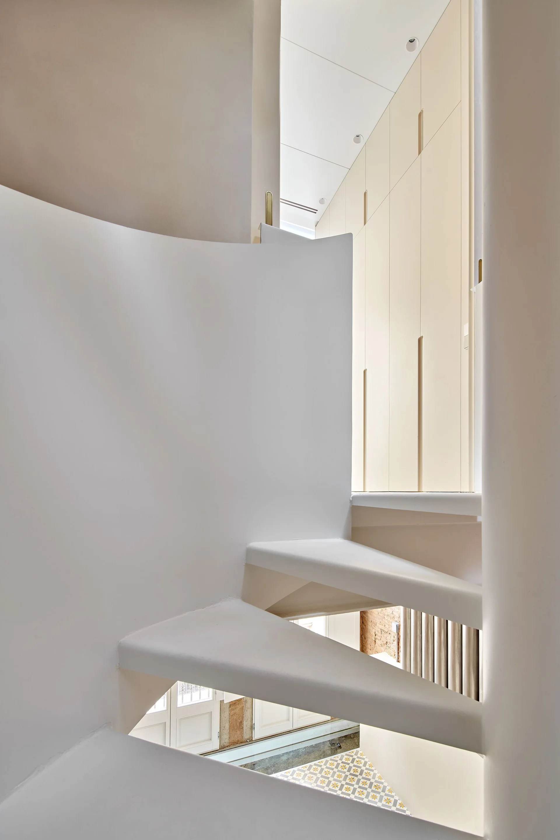An off-white spiral staircase with smooth curved plaster handrails rises next to light beige built-in cabinetry.
