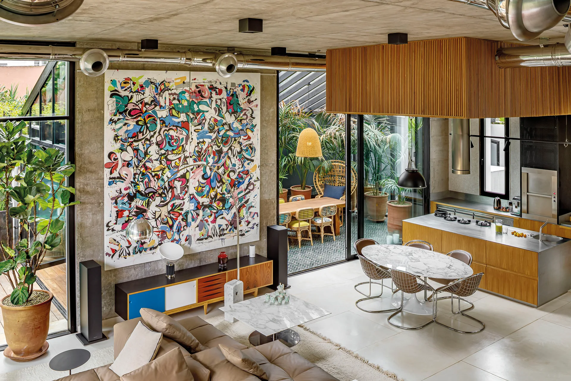 An open-plan living room with exposed concrete ceilings, a large colorful abstract painting on the wall, a leather sofa, and a kitchen area.