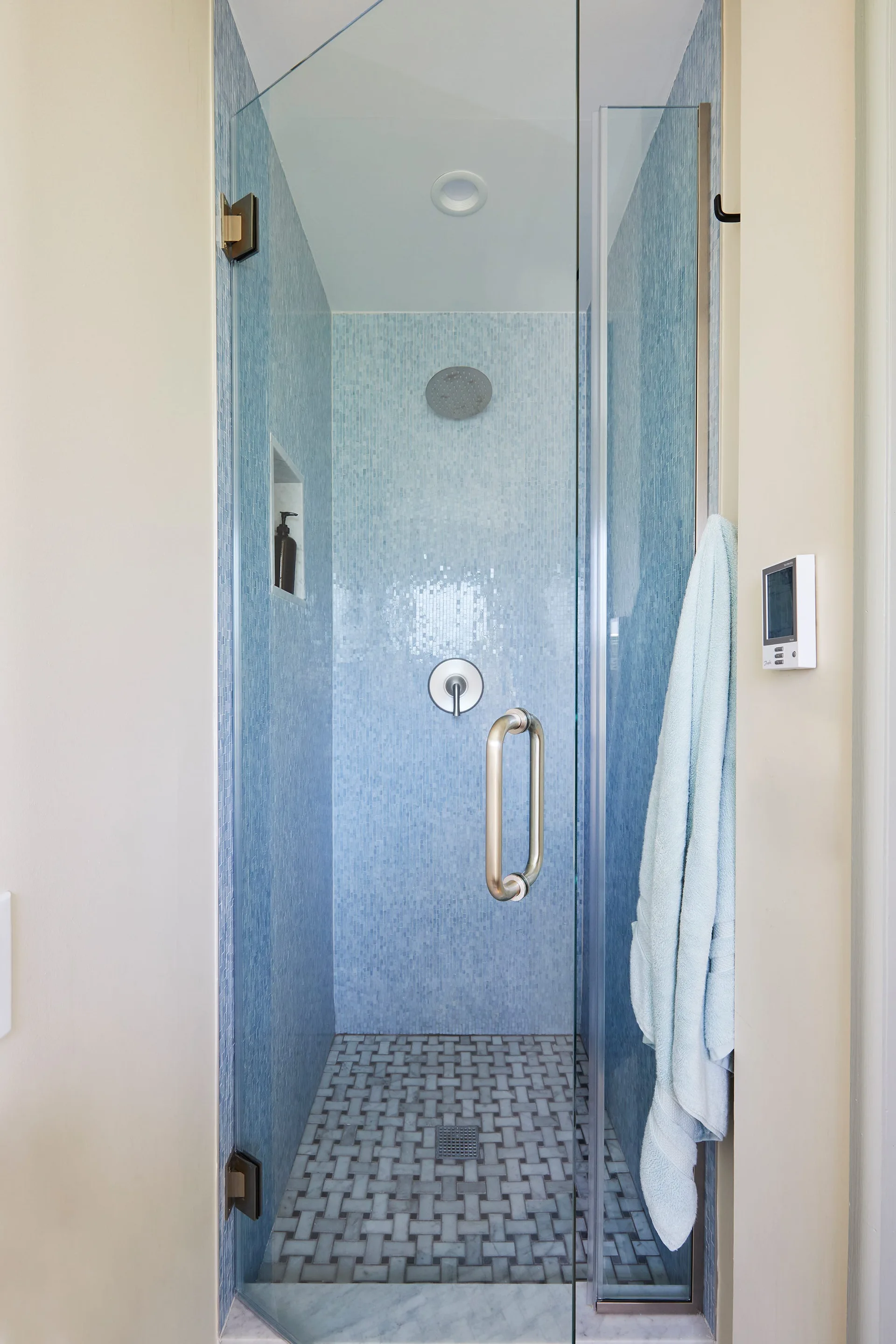 A walk-in glass shower enclosure features light blue mosaic tile walls and a grey and white basketweave pattern stone tile floor.