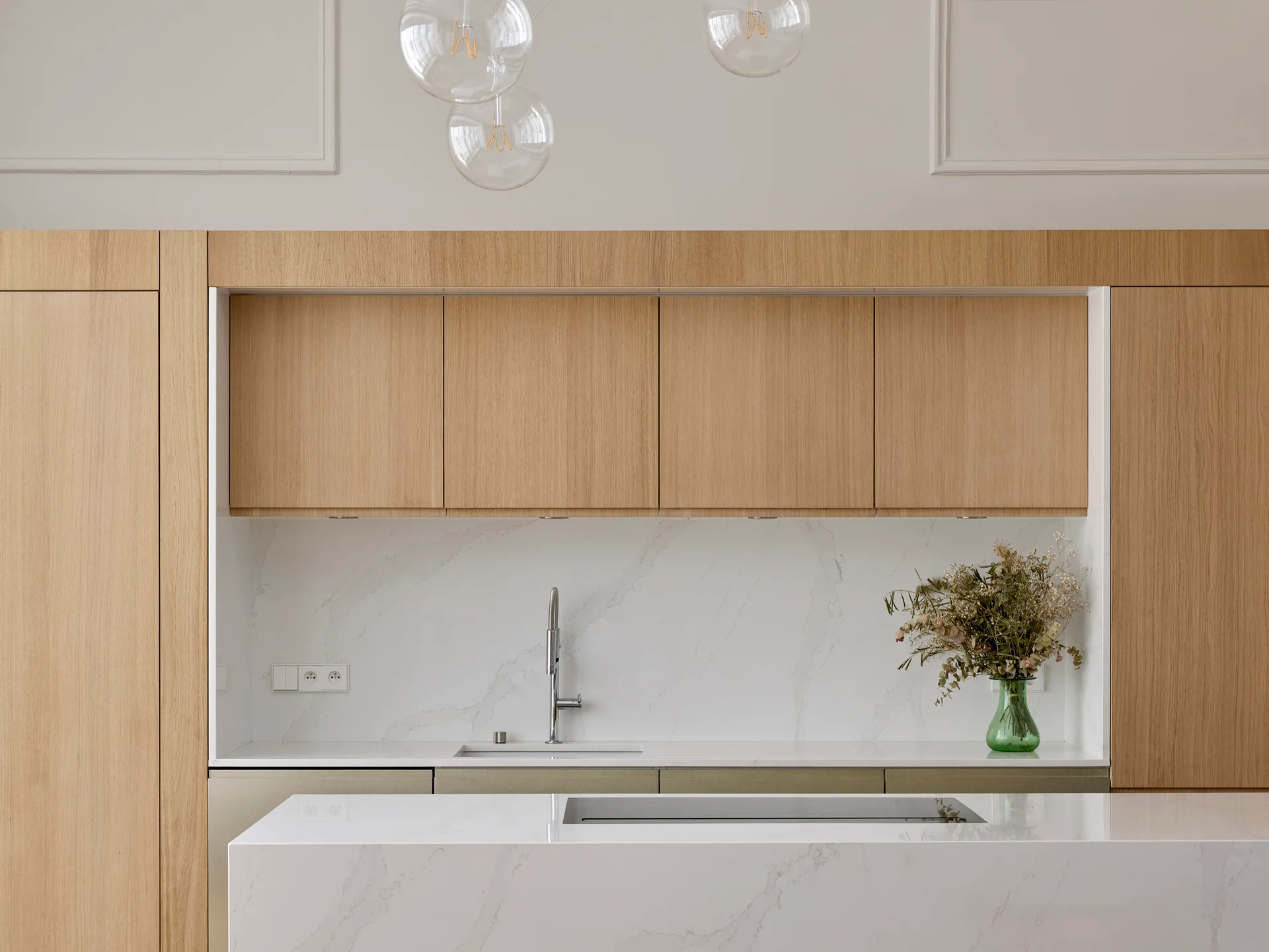 Minimalist kitchen showcasing flat-front light oak cabinets, a white veined stone backsplash, and a matching kitchen island.
