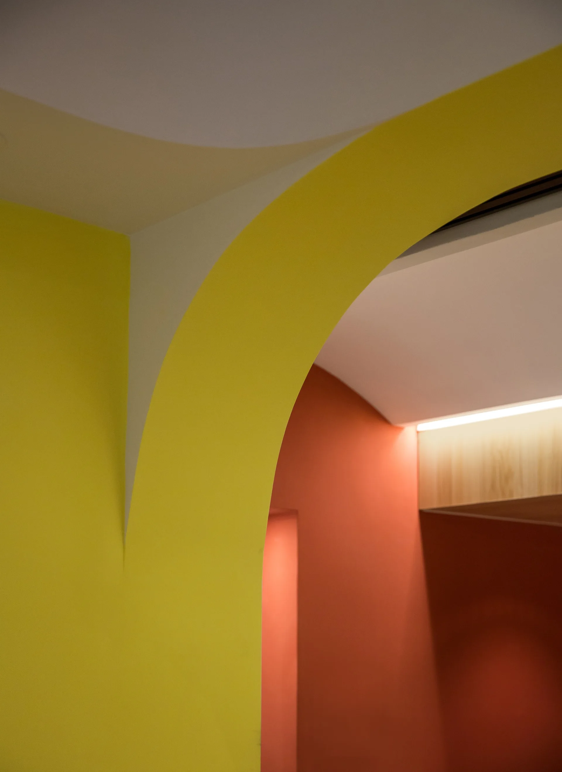 A close-up view of a bright yellow painted interior archway set against a warm terracotta orange wall with concealed warm lighting above.
