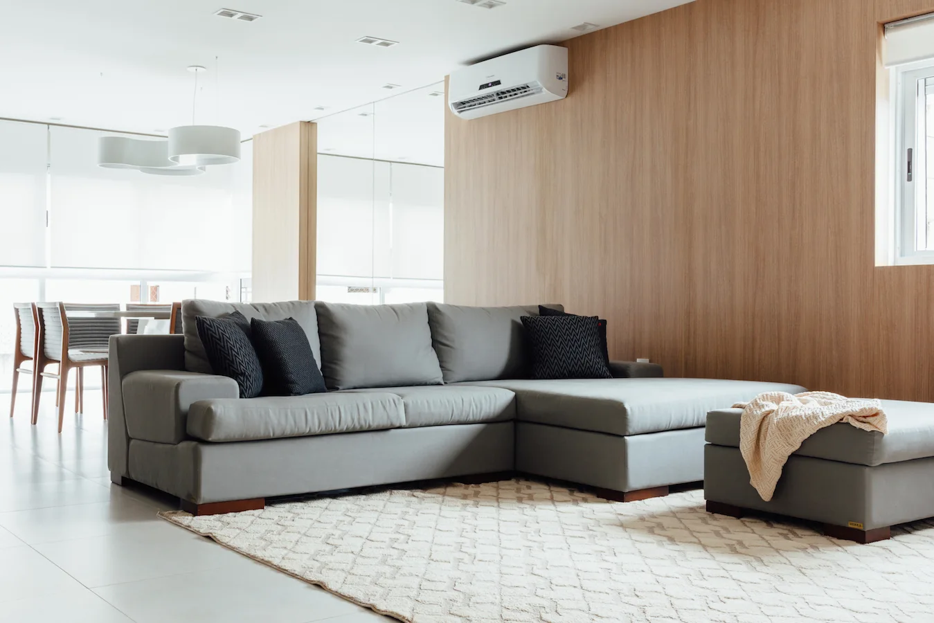 A contemporary living room features a large gray sectional sofa on a textured cream area rug in front of a wood-paneled accent wall.