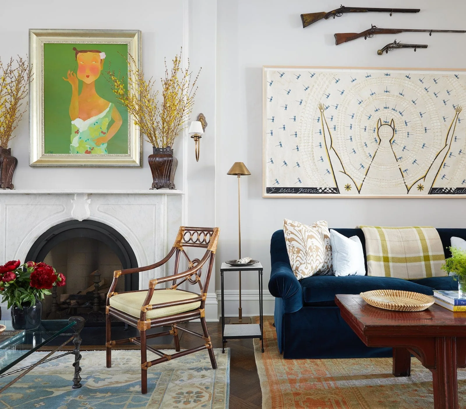 An eclectic living room featuring a white marble fireplace, a blue velvet sofa, layered patterned rugs, and framed artwork on the walls.
