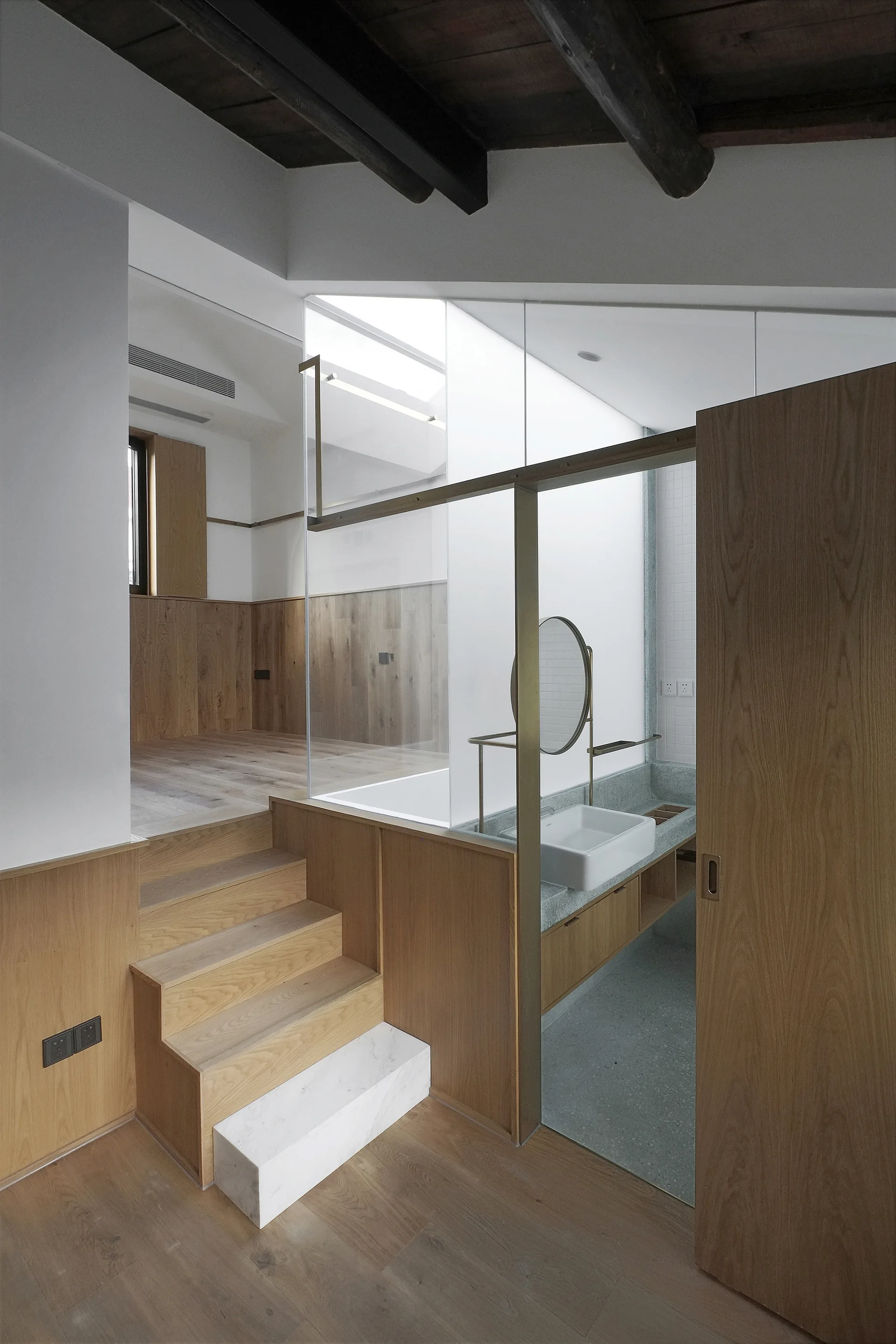 A modern split-level bathroom with wood-clad steps and platform, glass partition walls, and a stone-like vanity basin.
