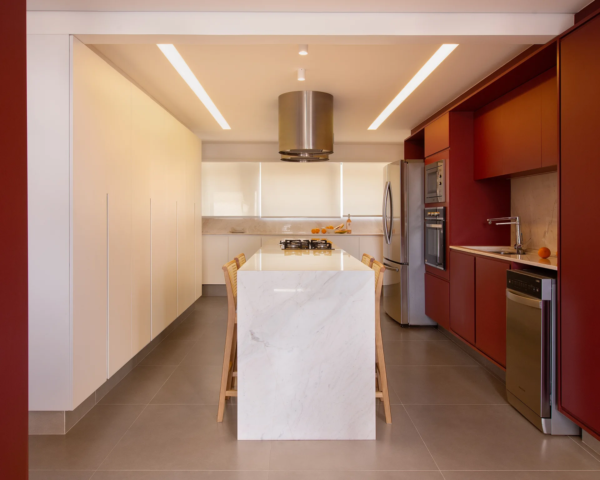A modern symmetrical kitchen with a marble-topped island, minimalist white cabinets, and deep red storage walls.