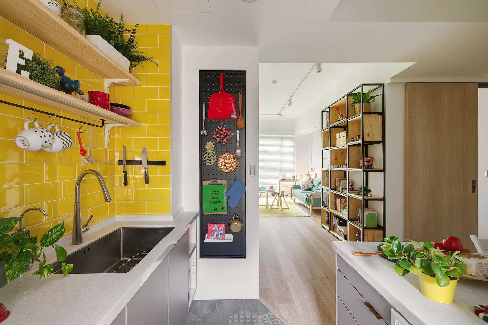 A kitchen sink area features a bright yellow subway tile backsplash, open wood shelving, and a black pegboard organizer on an adjacent wall.