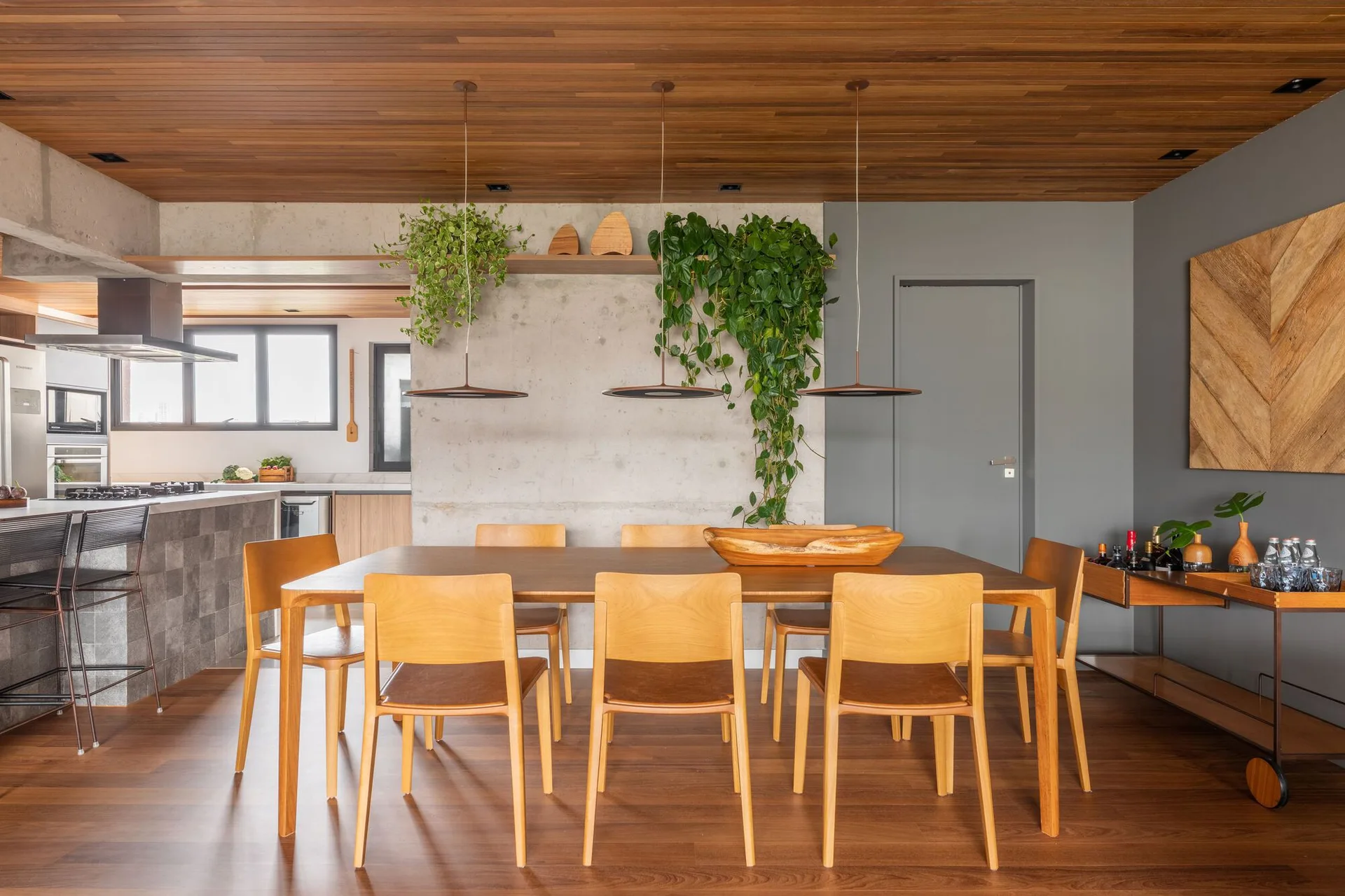 A contemporary dining room features a wooden dining table and chairs beneath a wood plank ceiling and next to an exposed concrete wall.