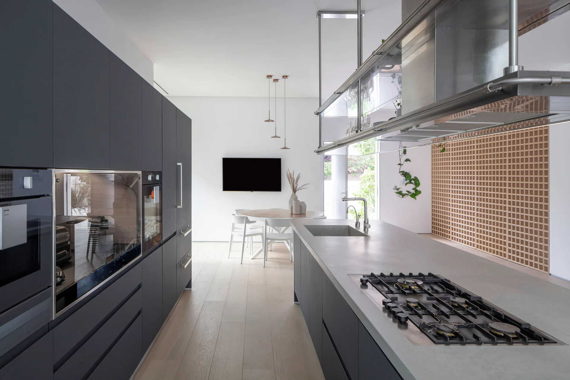 A modern kitchen with matte dark grey cabinets, a concrete-like island with a built-in cooktop, and a light wood floor leading to a dining area.