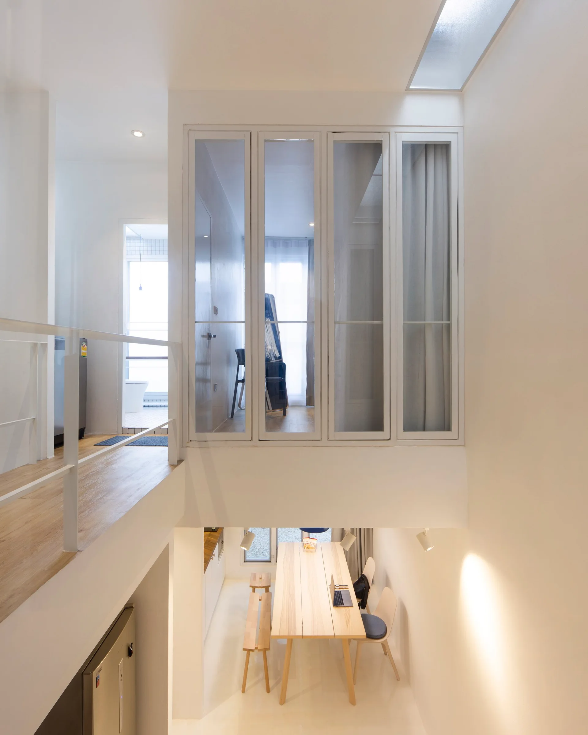 A split-level dining area features a light wood table on the lower floor and a loft corridor with a glass-paned partition above.