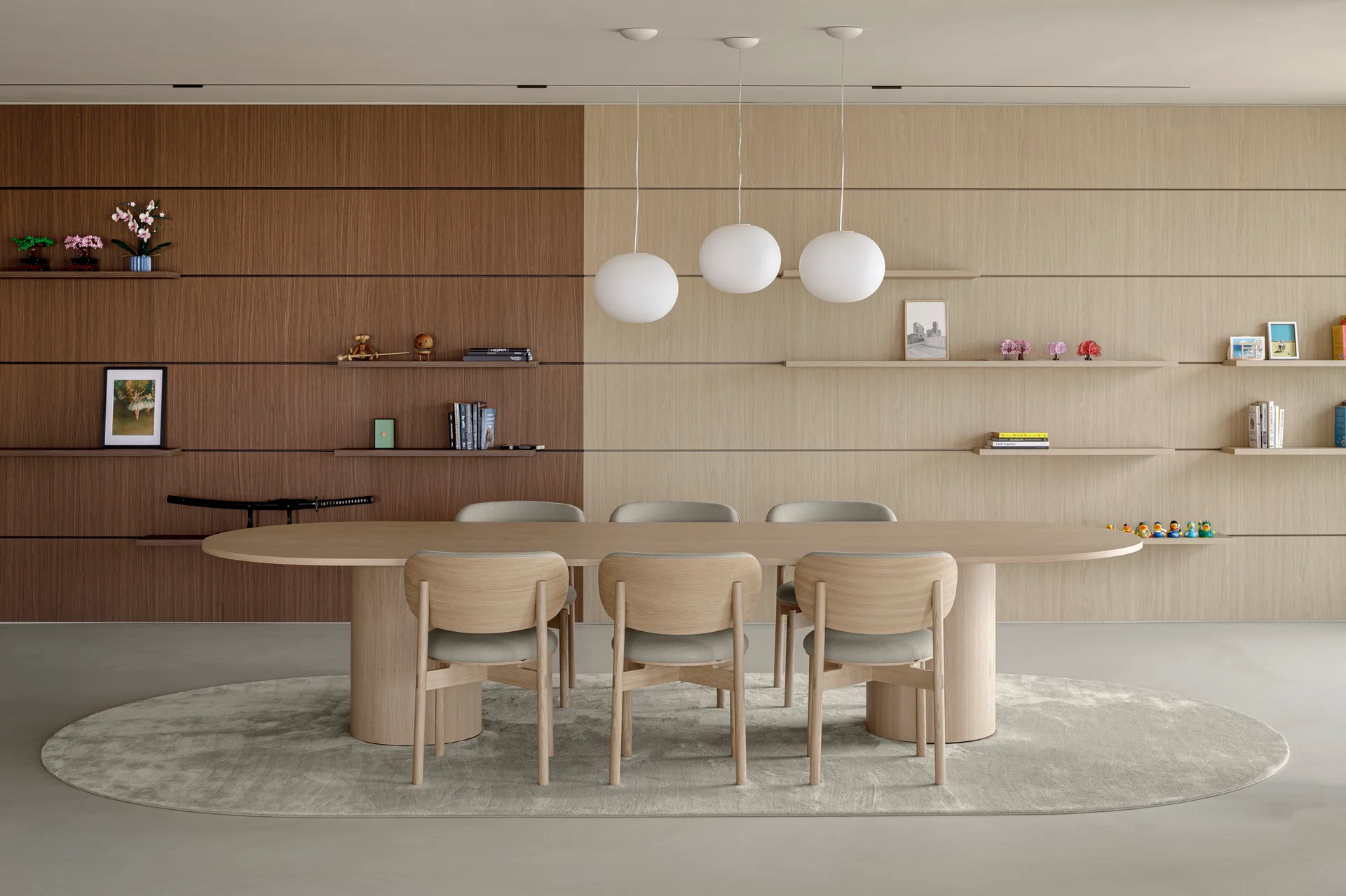 A minimalist dining room features an oval wooden table and chairs set on an oval rug beneath three spherical pendant lights against a two-tone wood wall.