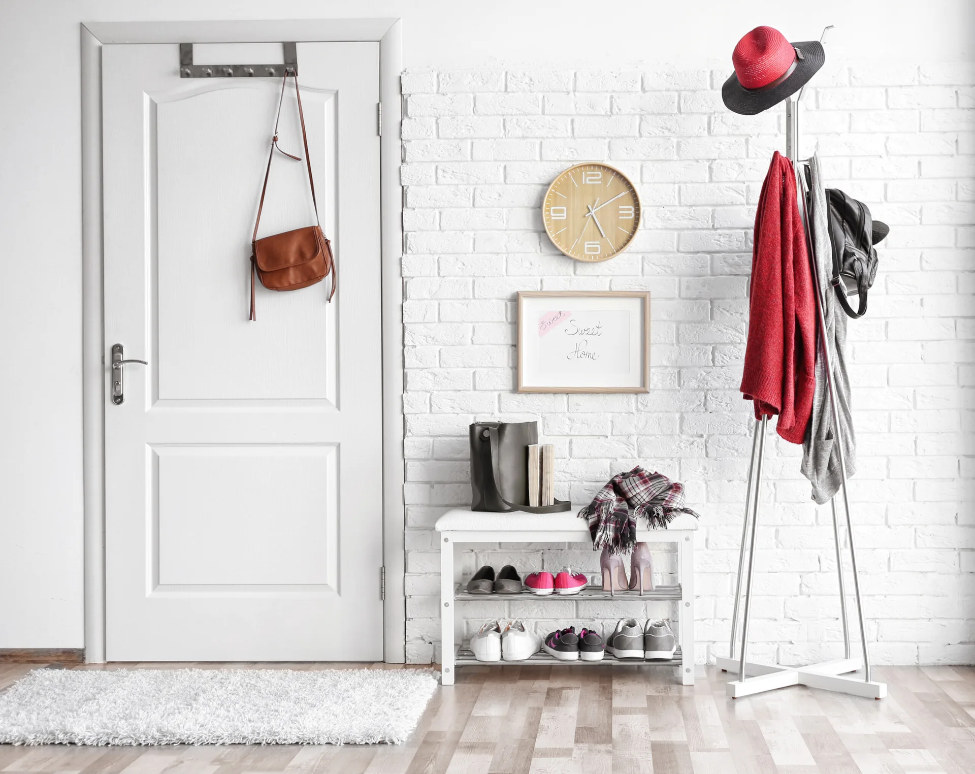A white painted brick entryway featuring a light wood floor, a white shoe storage bench, a metal coat rack, and a white paneled door.