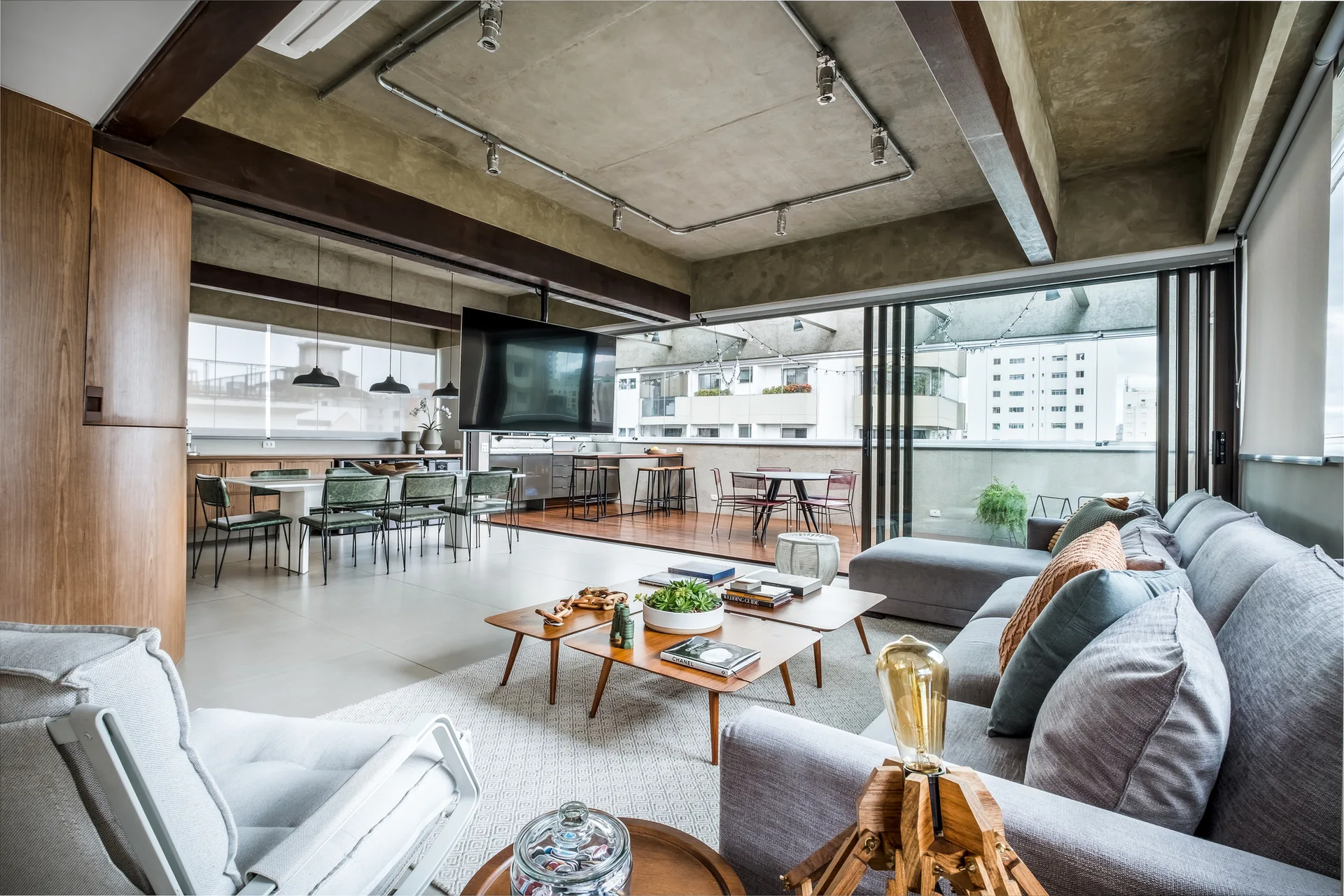An open living room featuring a concrete ceiling with exposed piping, a grey sectional sofa, and sliding glass doors opening to a balcony.