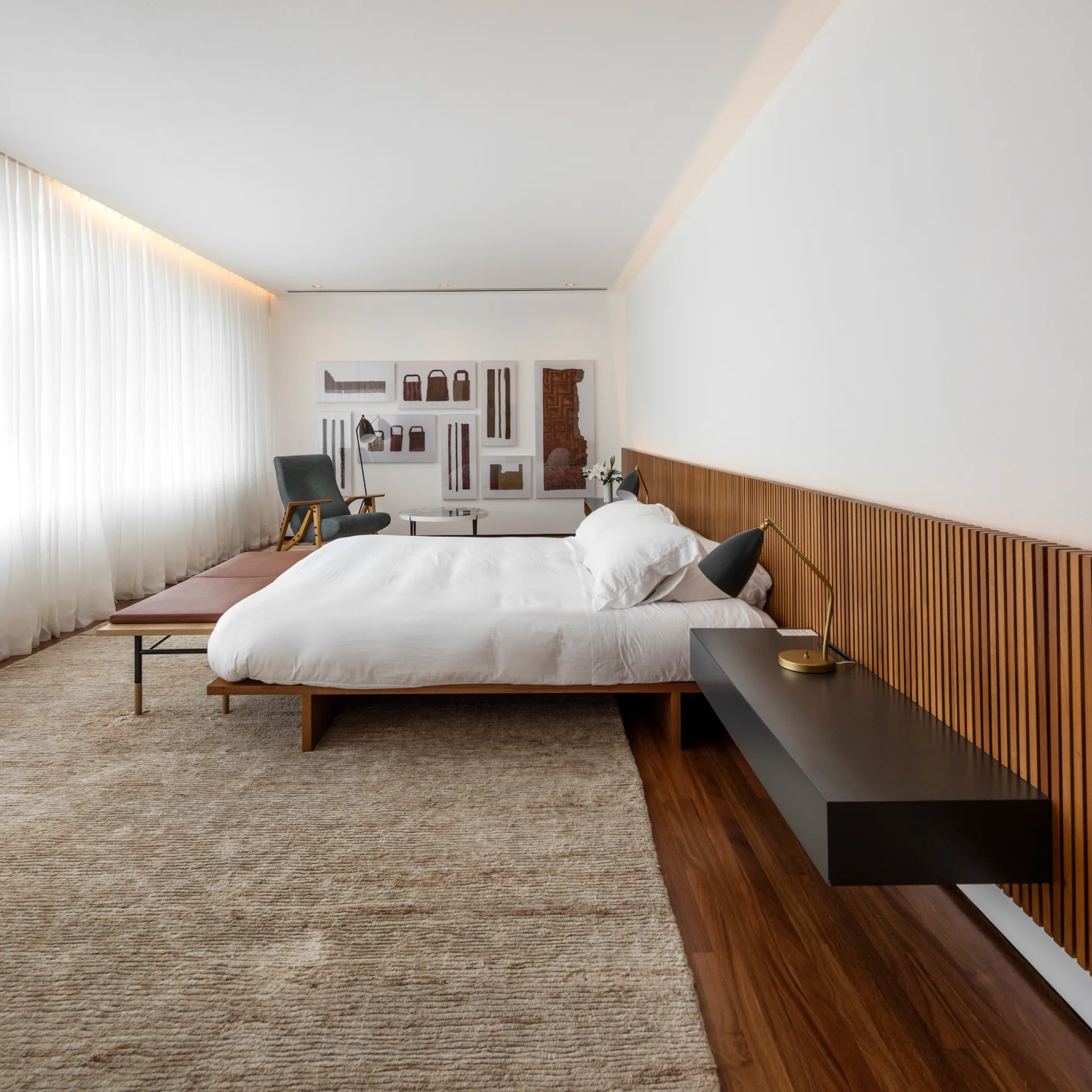 A minimalist bedroom featuring a low platform bed, a vertical wood slat accent wall, and a black floating nightstand on dark wood floors.