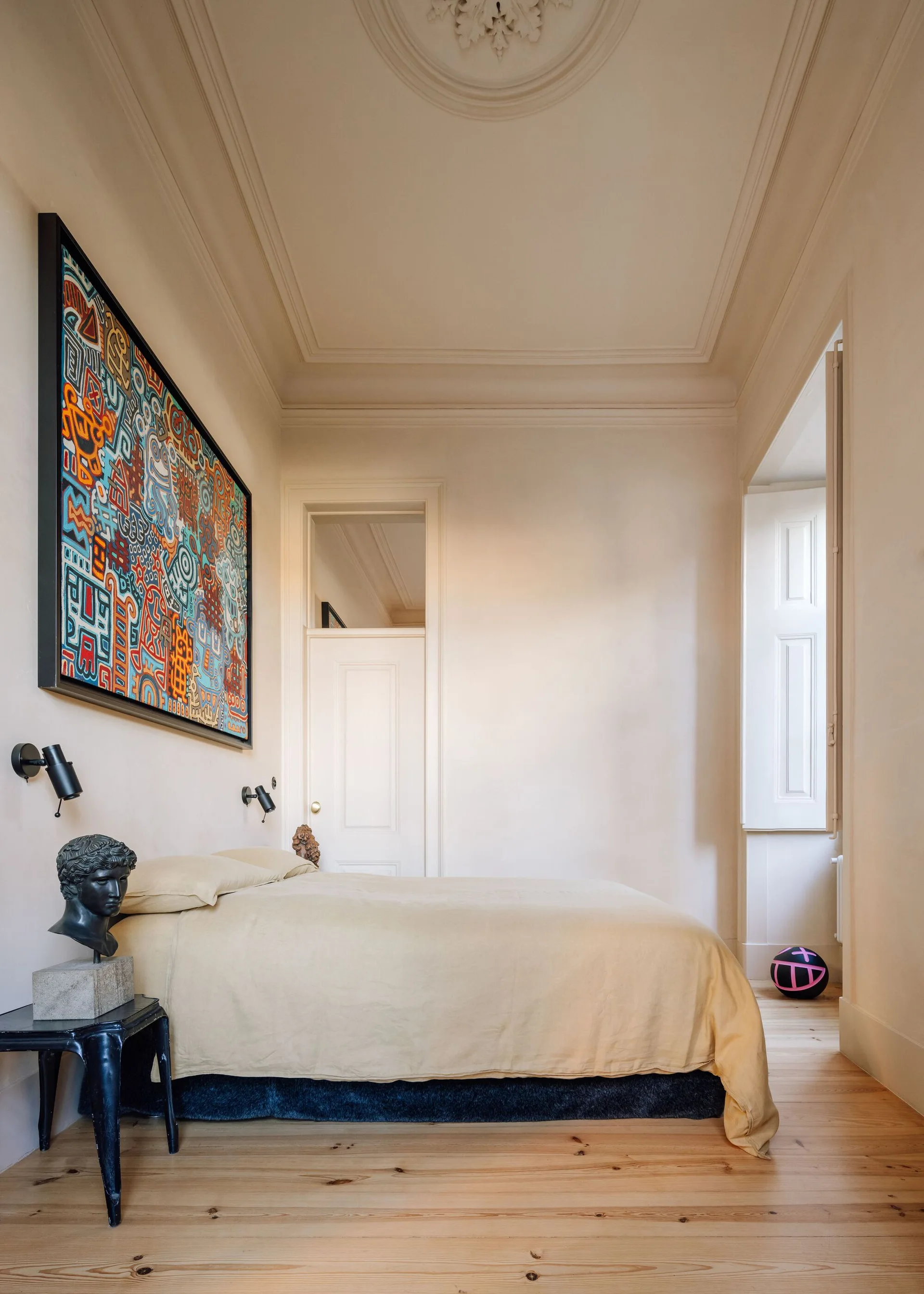 A bedroom with light wood floors, a low bed with yellow bedding, and a large colorful abstract painting on the wall.